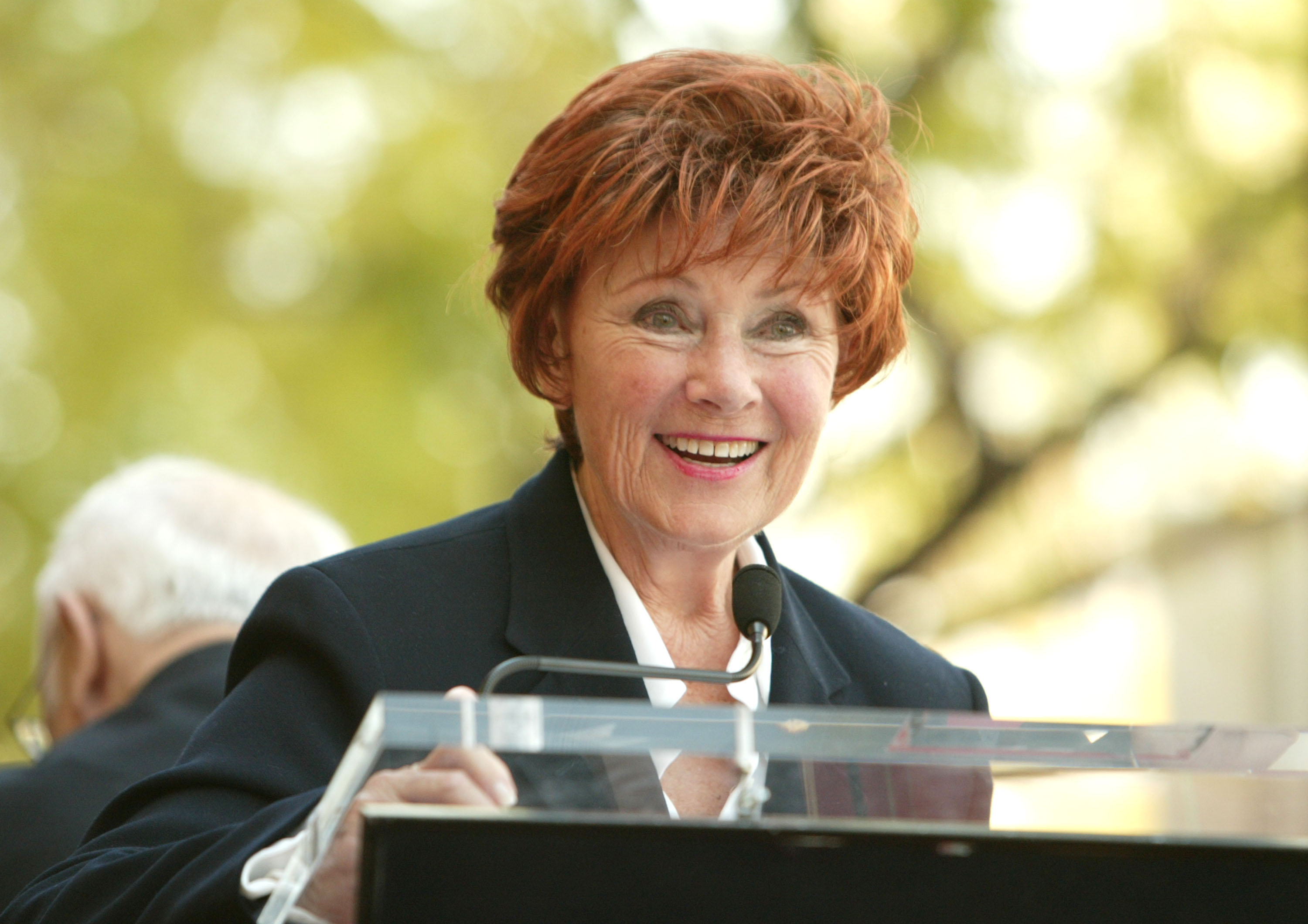 A photograph of actor Marion Ross addressing an audience from an outdoor lectern