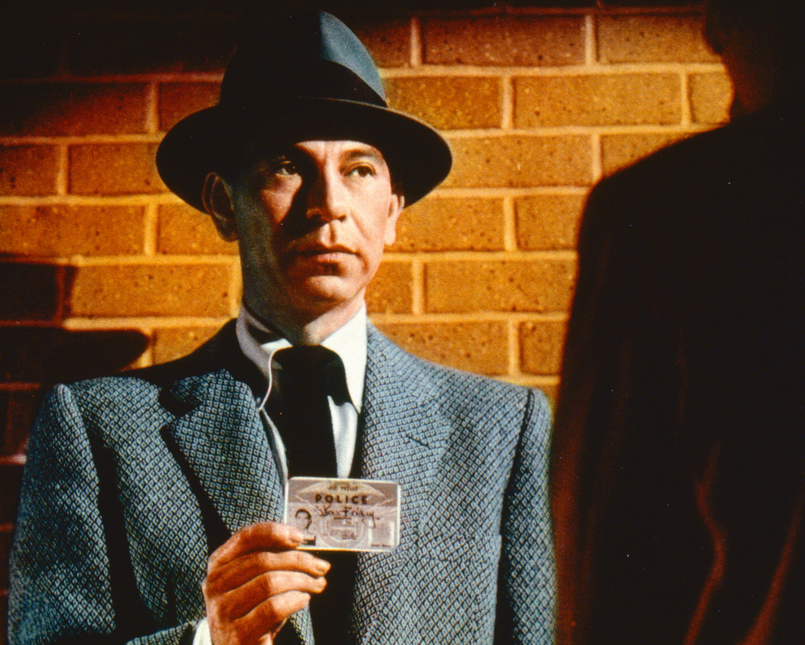 Actor Jack Webb poses as Sergeant Joe Friday wearing a grey jacket and a grey fedora, with a black band, while holding up his warrant card in a publicity still issued for the US television series, 'Dragnet', 1955