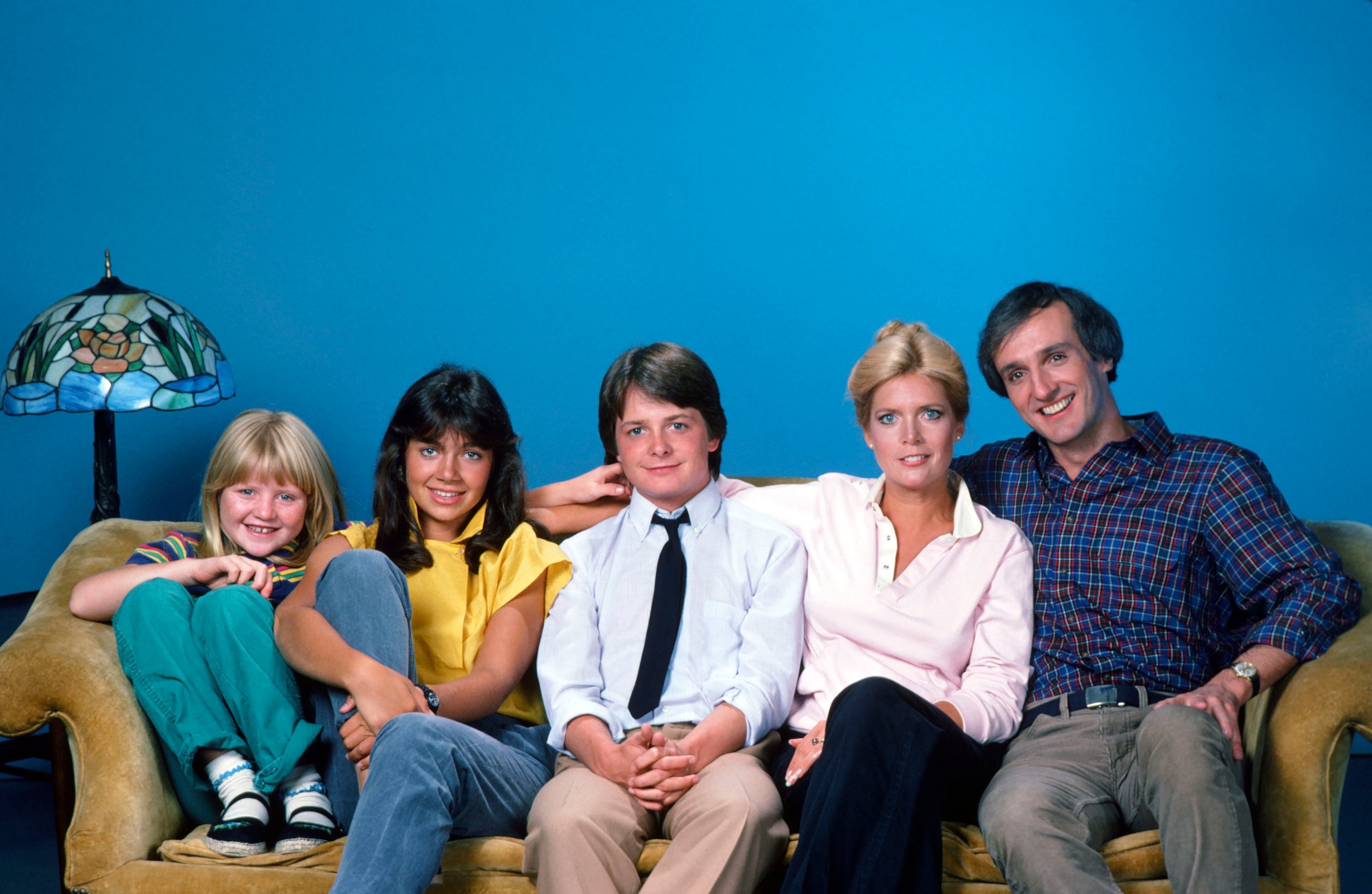 The cast of 'Family Ties' sits together on a couch in 1982: (L to R): Tina Yothers as Jennifer Keaton, Justine Bateman as Mallory Keaton, Michael J. Fox as Alex P. Keaton, Meredith Baxter as Elyse Keaton, and Michael Gross as Steven Keaton