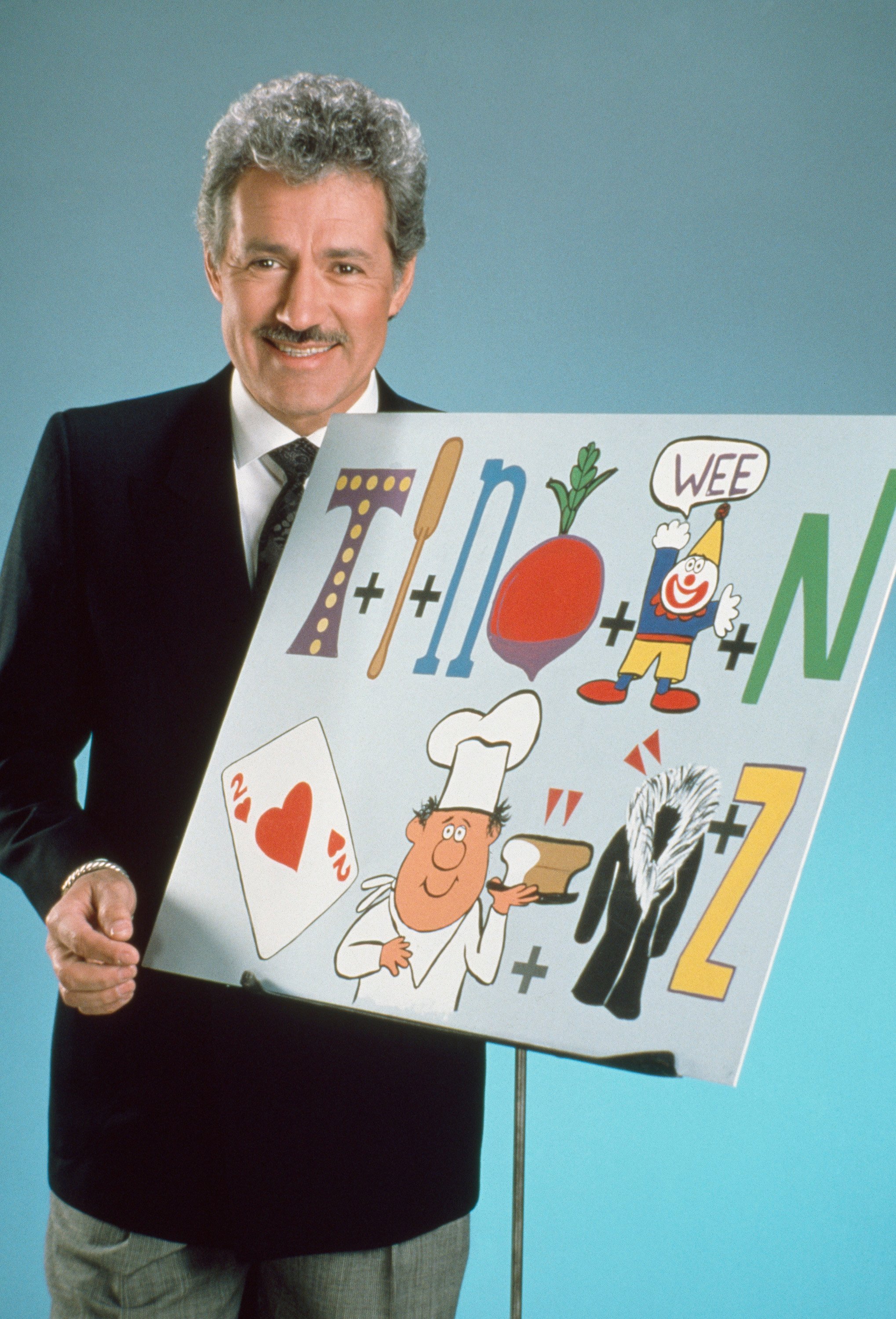 Alex Trebek poses while he holds a 'Classic Concentration' puzzle