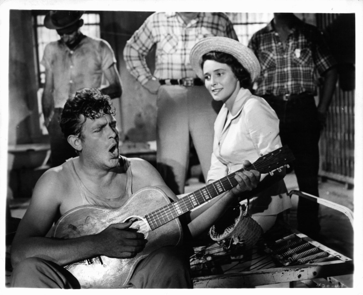 Andy Griffith (left) plays guitar as Patricia Neal watches smiling in a scene from 1957's 'A Face in the Crowd'