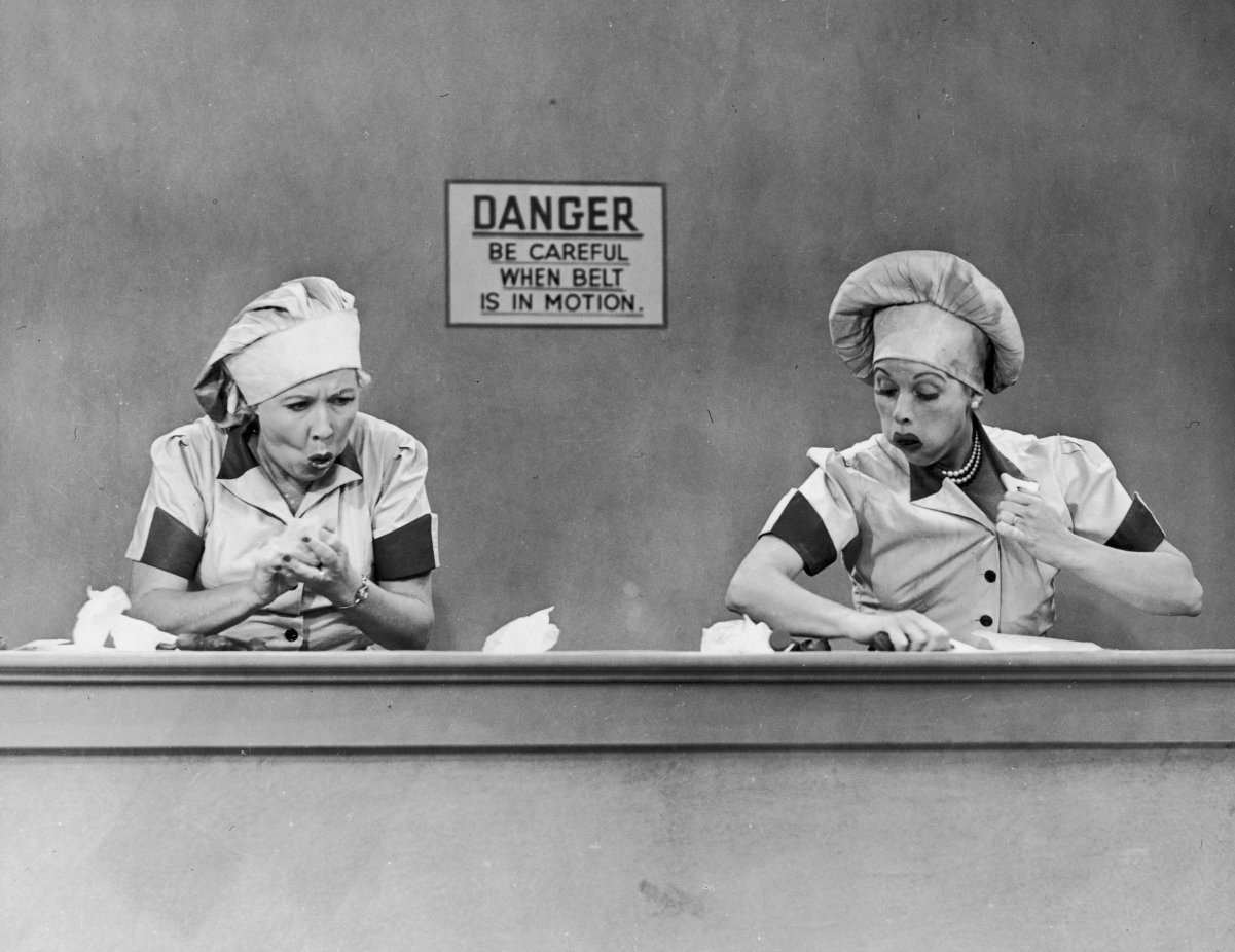 (L to R): 'I Love Lucy' stars Vivian Vance and Lucille Ball dressed in candy-maker uniforms hiding unwrapped candies in the classic 'Job Switching' episode, 1952