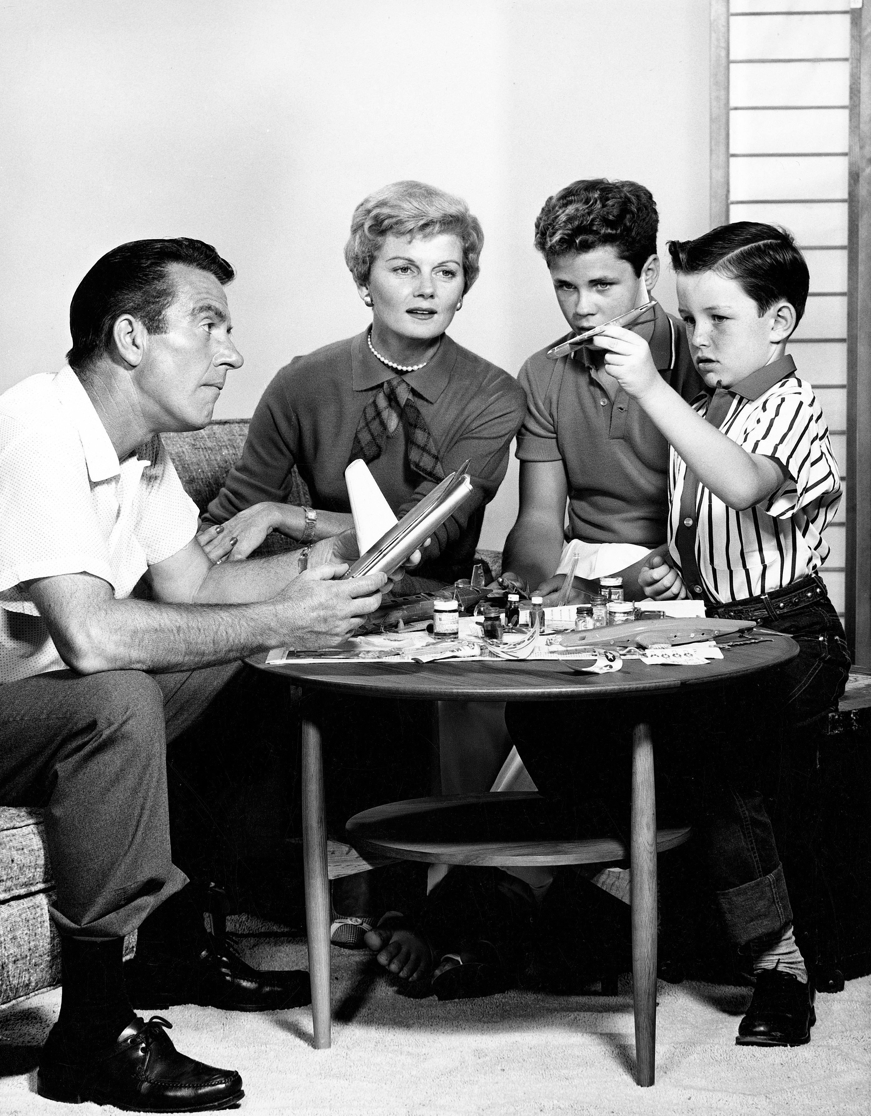 The cast of 'Leave It to Beaver' sit together as the Cleaver boys assemble a model airplane: (L to R): Hugh Beaumont, Barbara Billingsley, Tony Dow, and Jerry Mathers