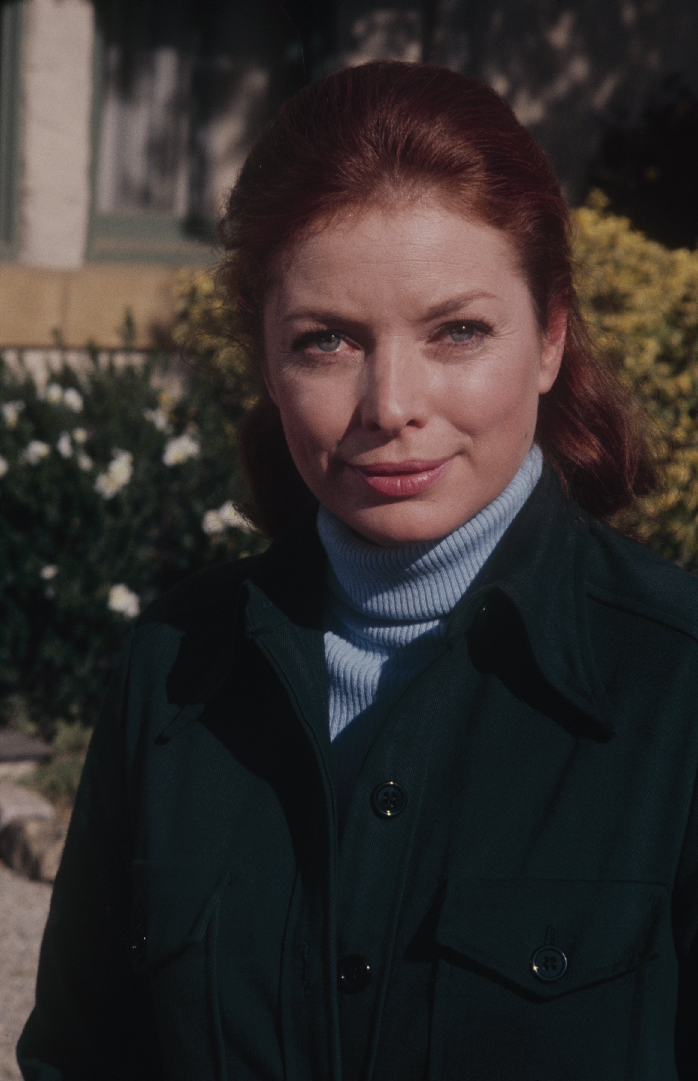 Actor Aneta Corsaut poses for a photo in a blue turtleneck, dark jacket, and her red hair pulled back, 1973