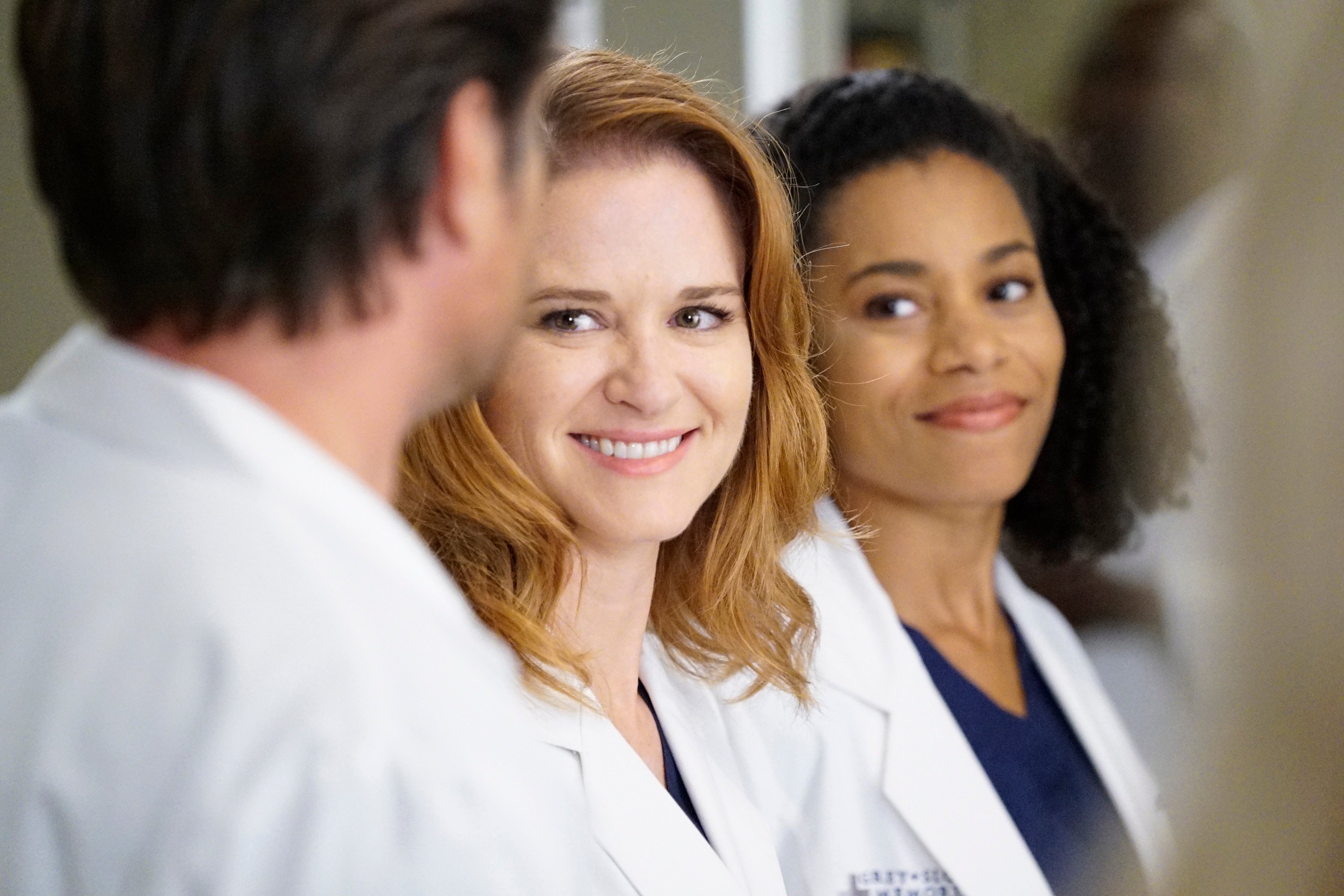 Grey's Anatomy stars Sarah Drew and Kelly McCreary smiling on set.