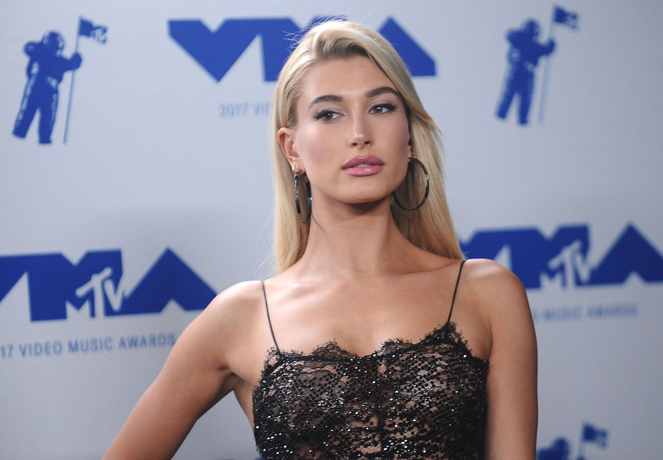 Hailey Bieber standing in front of a blue and white background