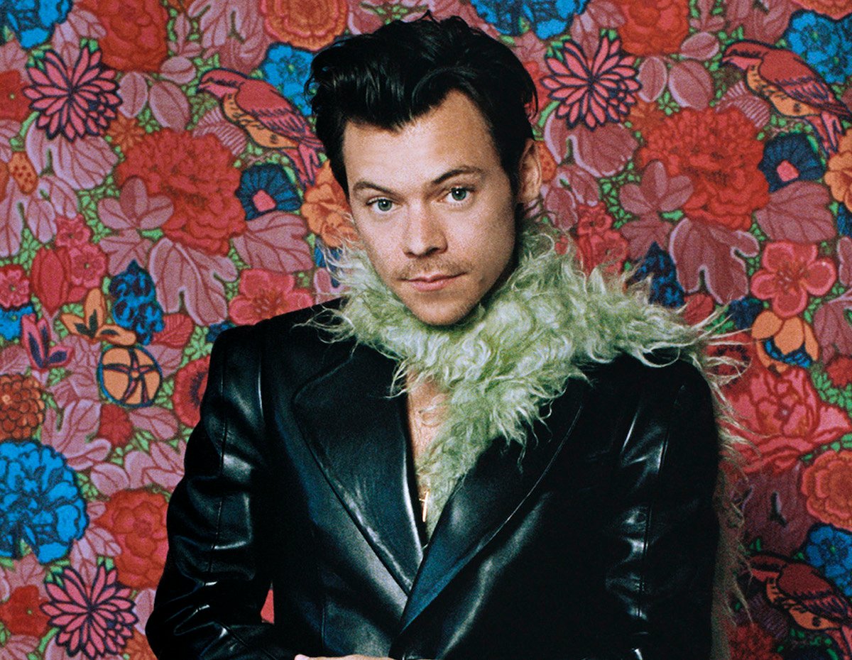 Harry Styles in a leather jacket and green boa in front of a floral background at the 2021 GRAMMY Awards | Anthony Pham/Getty Images