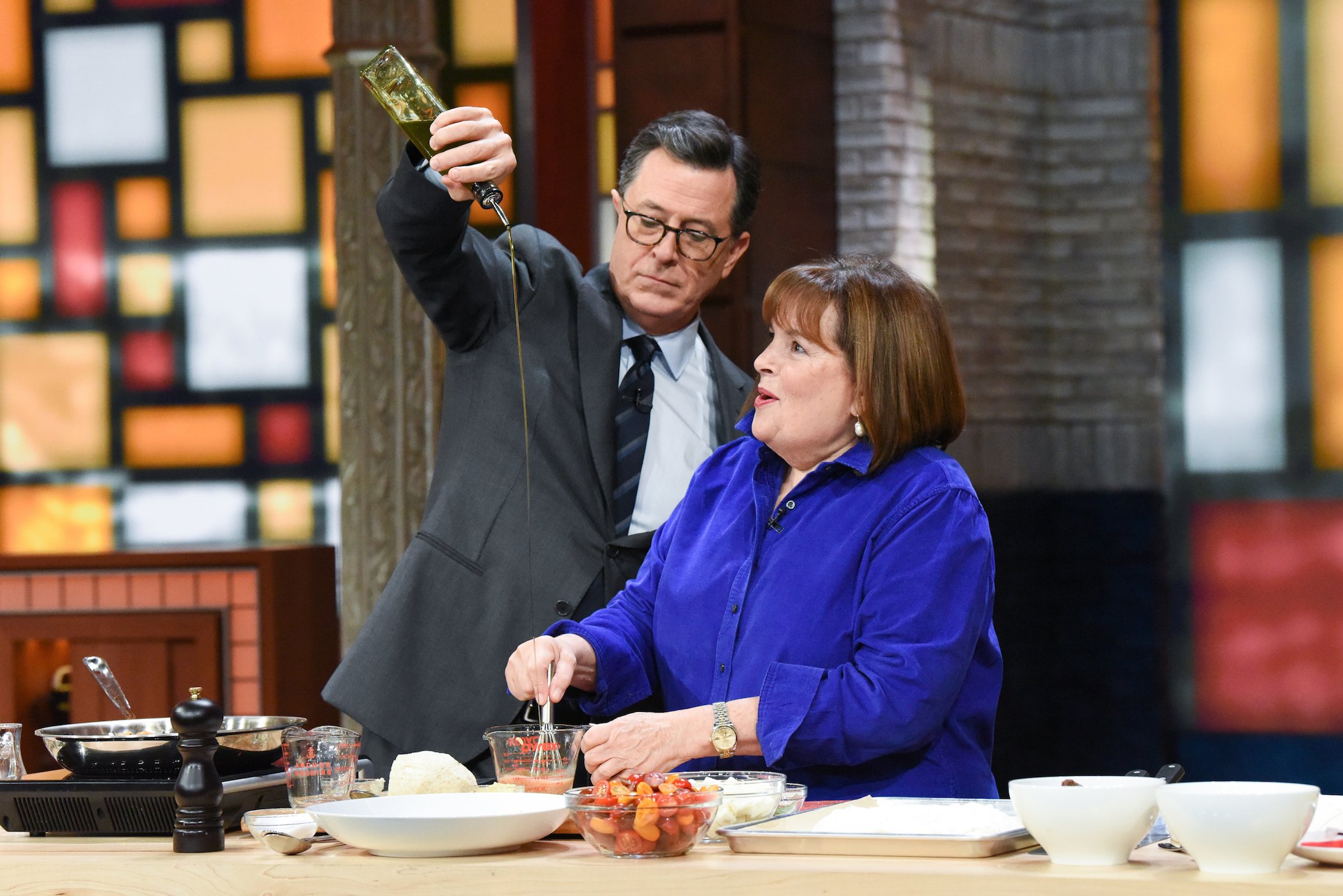 Ina Garten cooks with Stephen Colbert, seen pouring oil