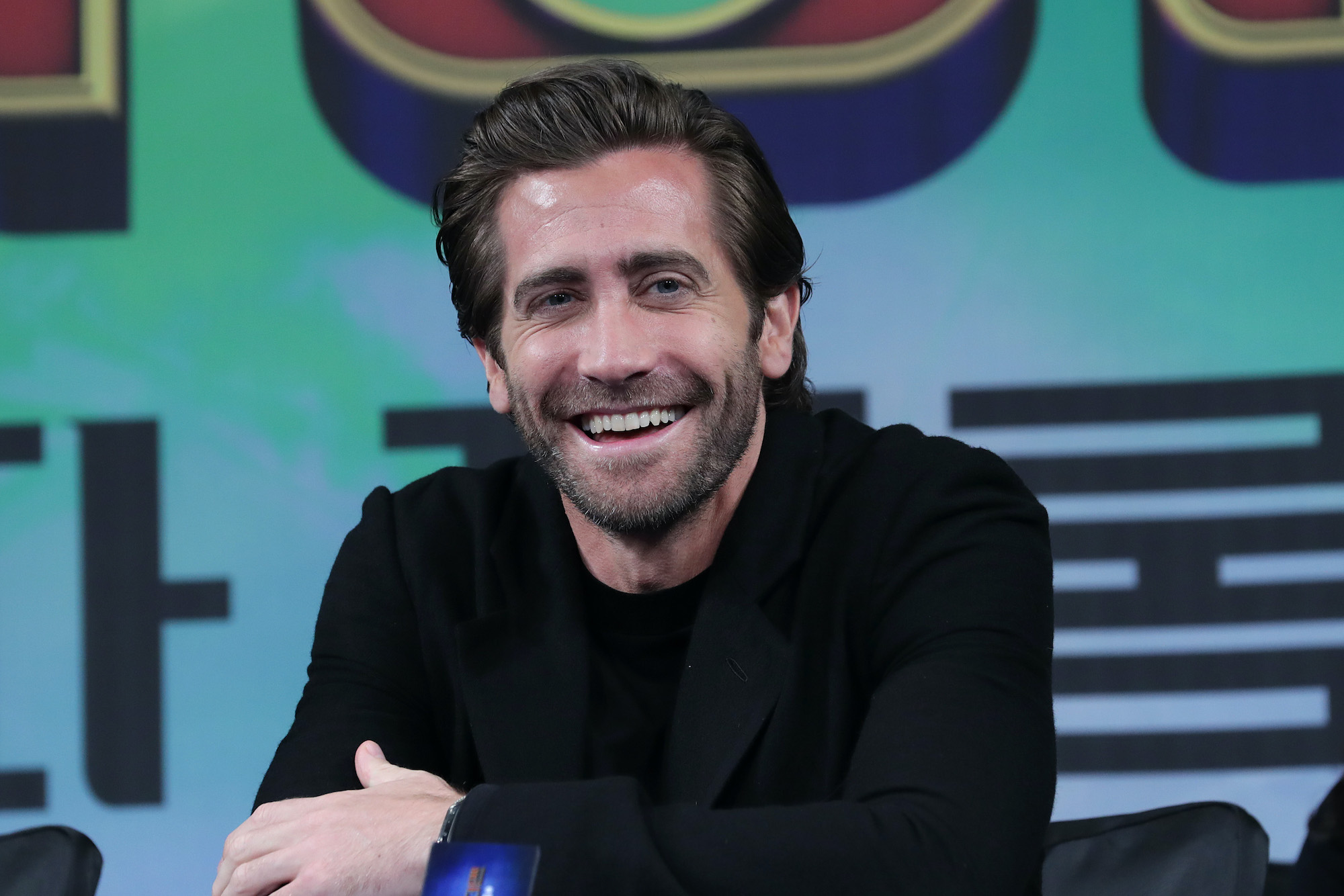 Jake Gyllenhaal smiling in front of a blue background