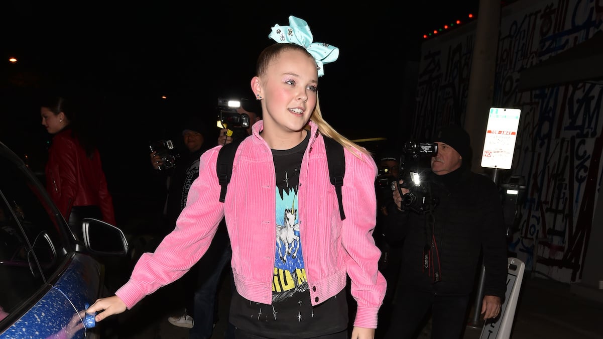 JoJo Siwa in a pink jacket and blue bow walking to her car