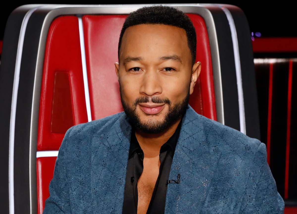 John Legend sitting in a red chair wearing a blue blazer and black shirt on set of 'The Voice' | Trae Patton/NBC/NBCU Photo Bank via Getty Images