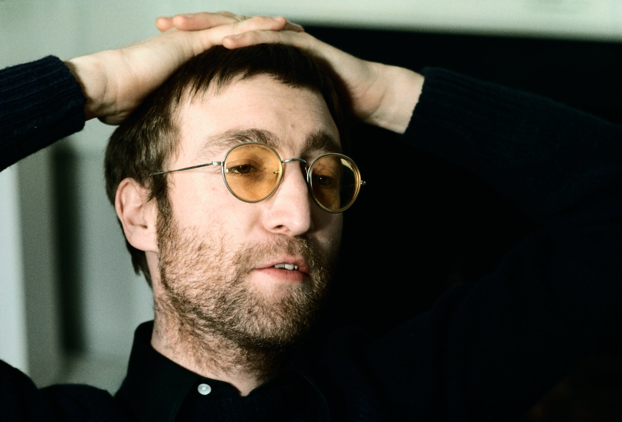 John Lennon wearing yellow glasses with his hands on his hand