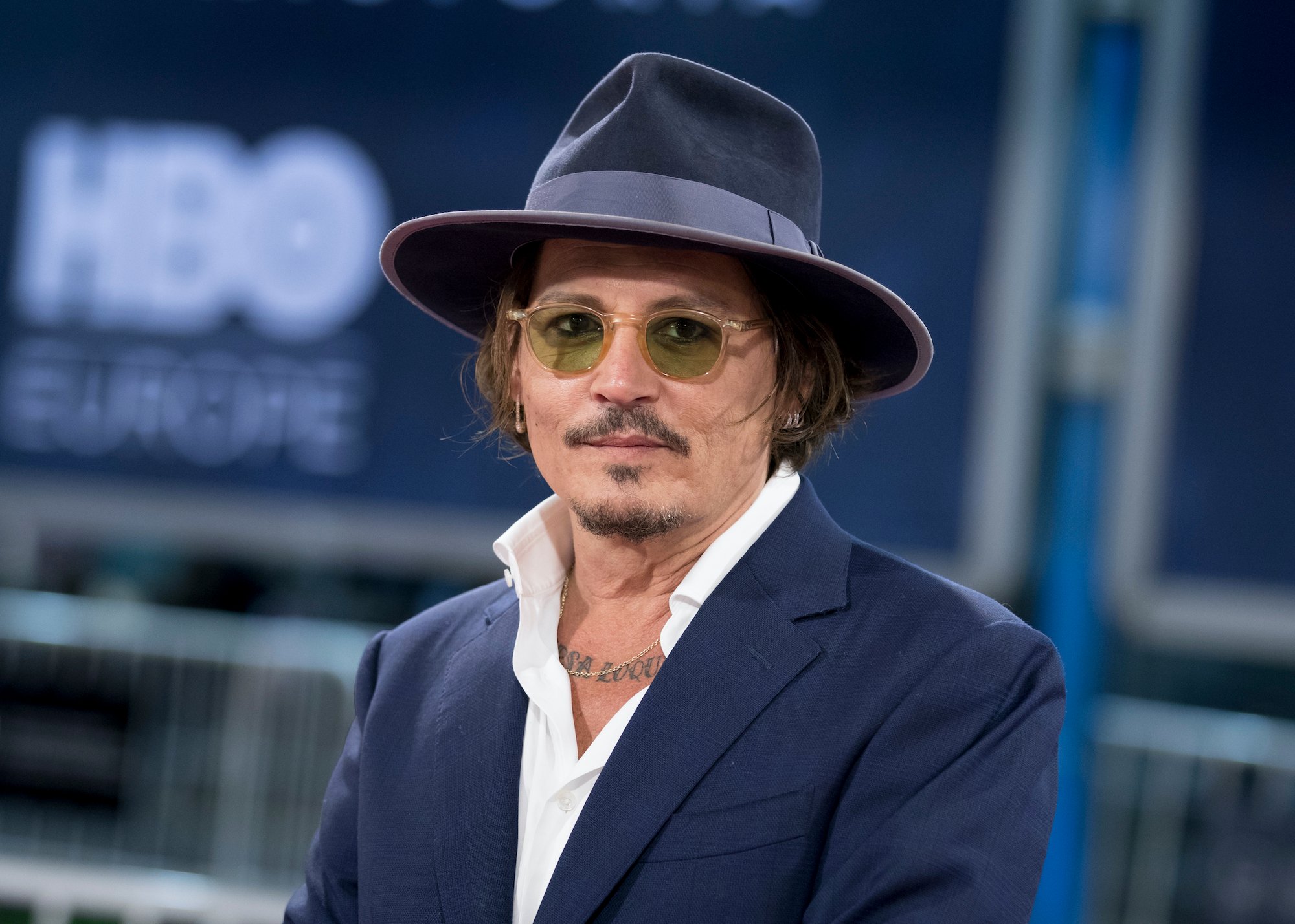 Johnny Depp in a hat and glasses in front of a blurred blue background