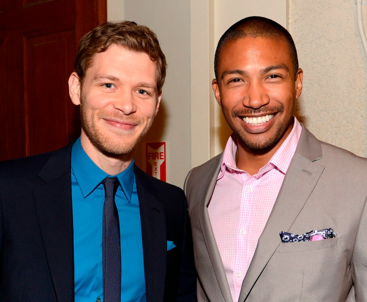 Joseph Morgan in a blue shirt and black suit and Charles Michael Davis in a pink shirt and tan suit smile for a picture at The CW's 2013 Upfront
