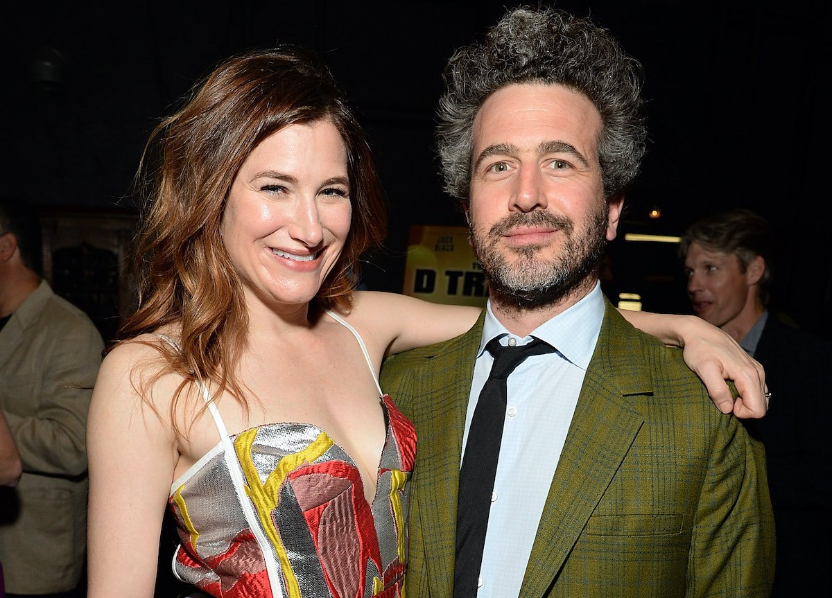 Kathryn Hahn in a multicolored dress wraps her arm around her, husband Ethan Sandler, wearing a plaid green blazer | Michael Kovac/WireImage