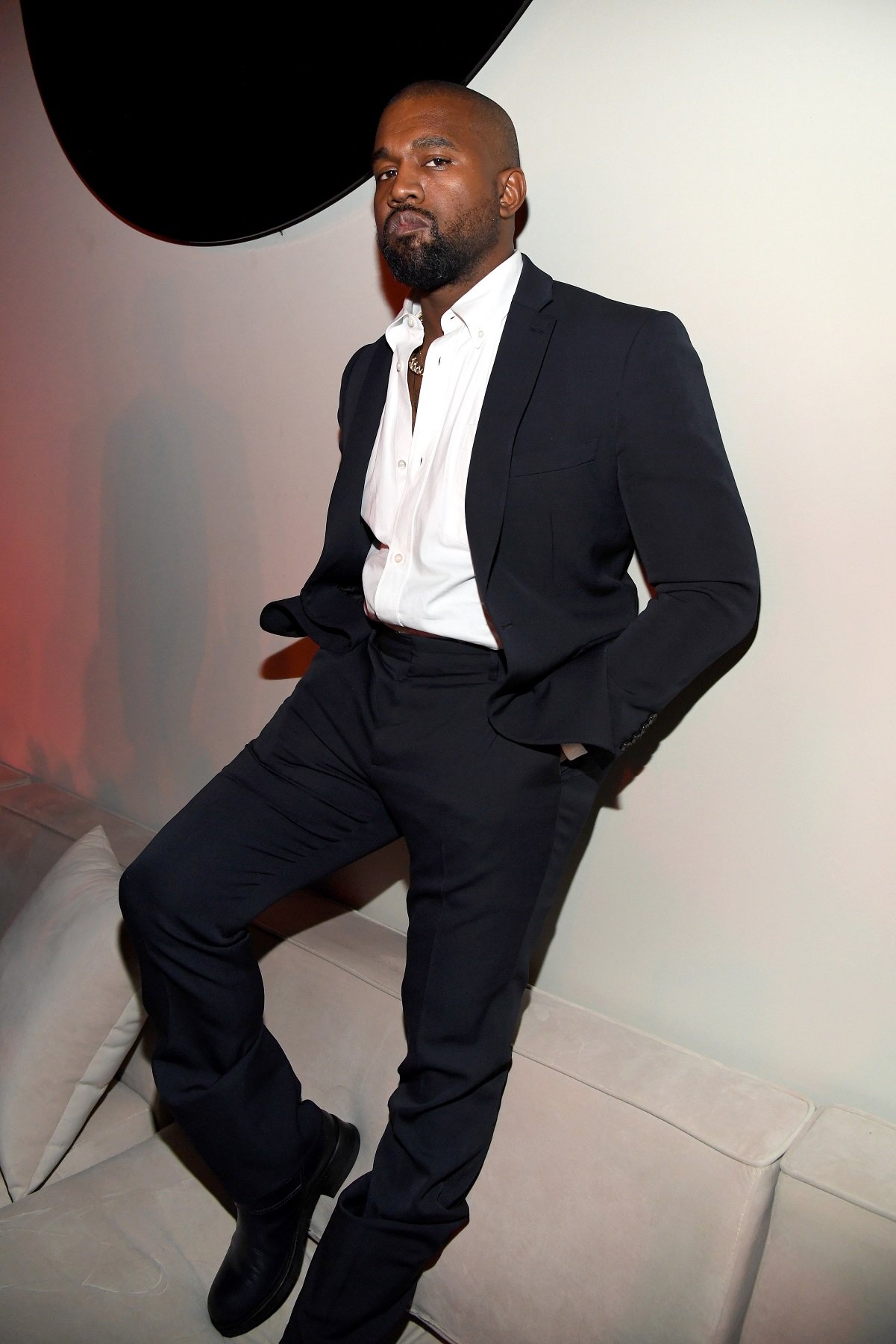 Kayne West dressed in a suit and standing on a couch at Sean Combs' 50th birthday party