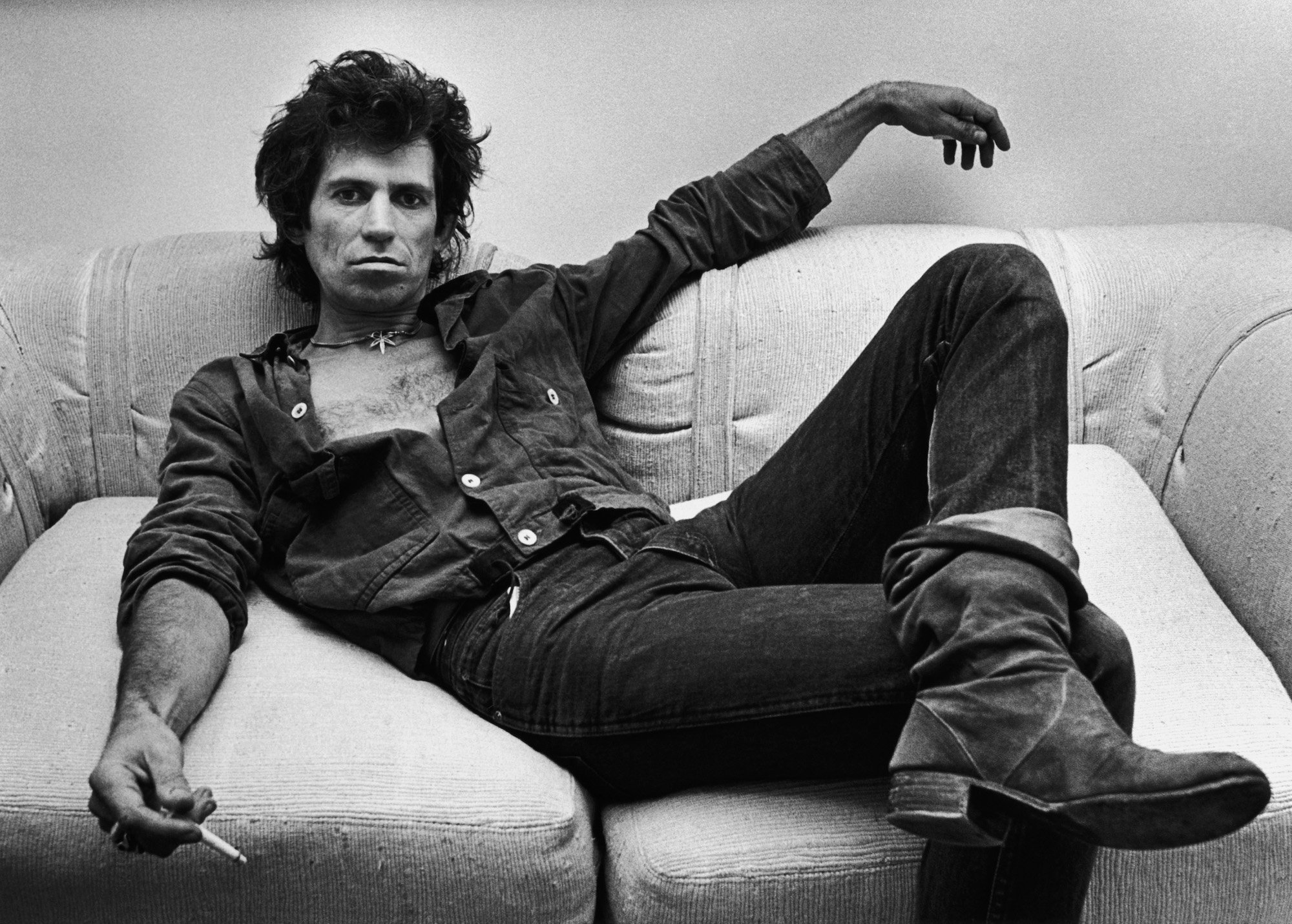 Keith Richards sitting on a couch, holding a cigarette, in black and white