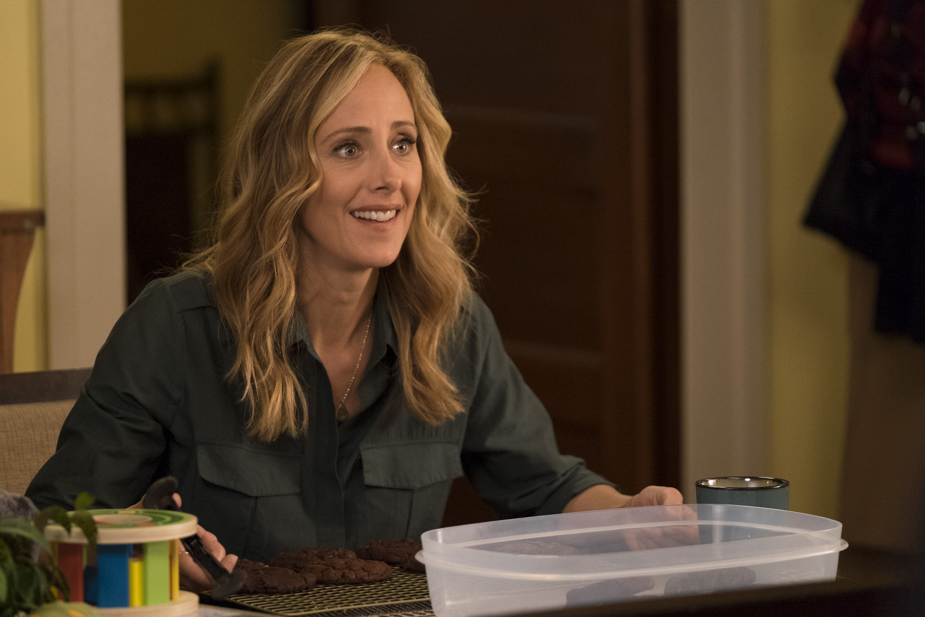 Kim Raver wearing a dark green sweater sitting at a table in a scene from 'Grey's Anatomy'