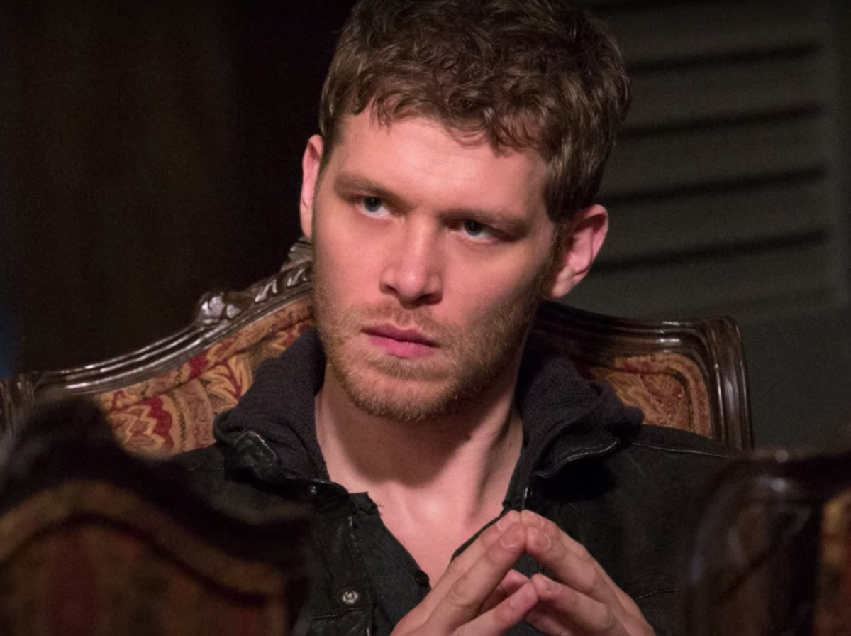 Joseph Morgan as Klaus Mikaelson sitting in an ornate chair and pressing his fingertips together with a stern look on his face in a scene from 'The Originals'