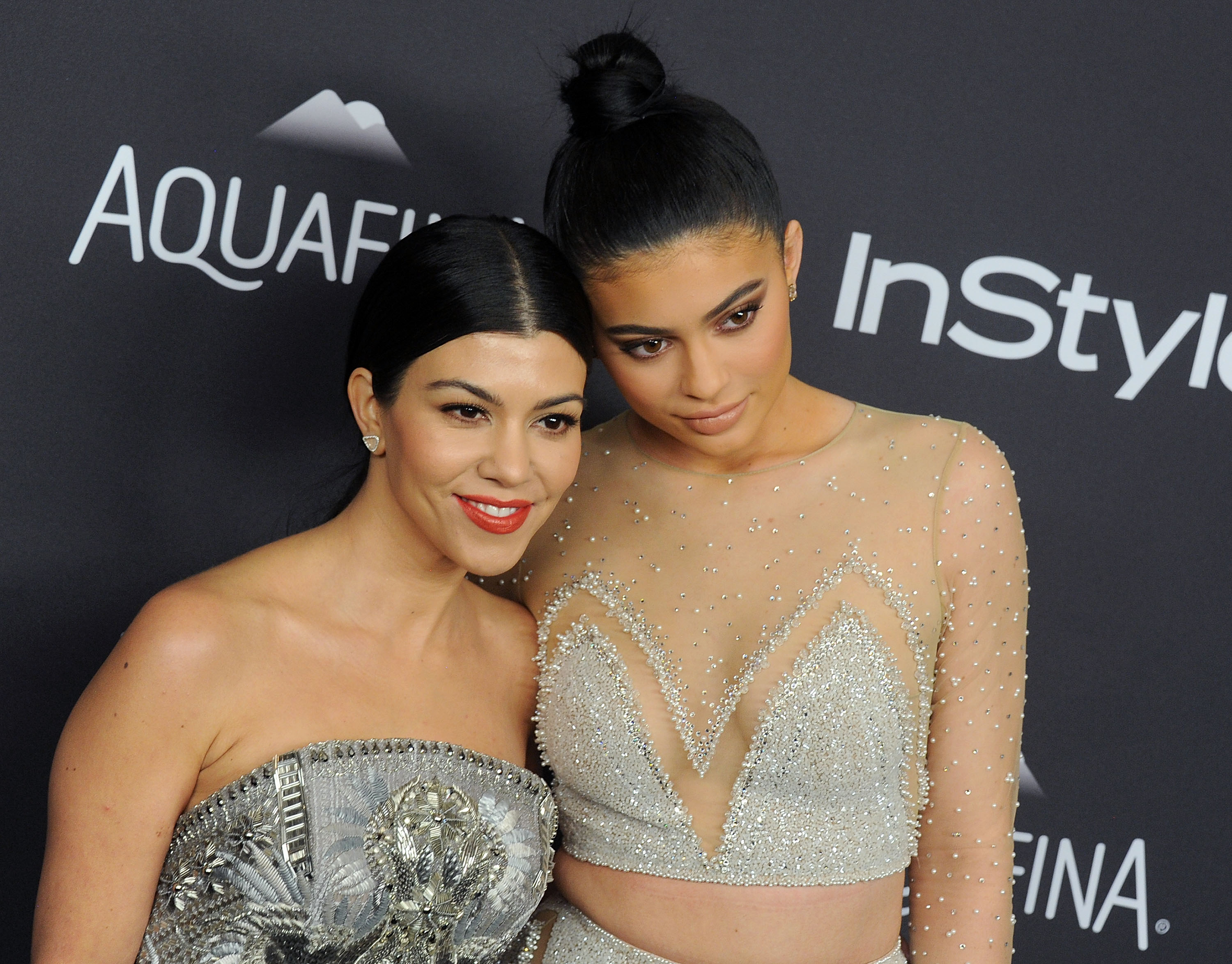 Kourtney Kardashian and Kylie Jenner posing next to each other in front of a black backdrop