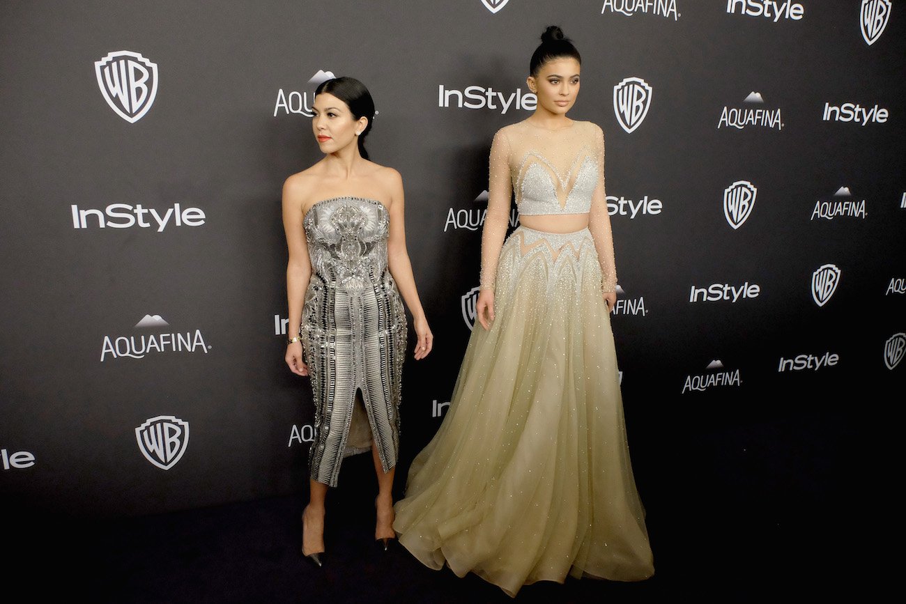 Kourtney Kardashian and Kylie Jenner posing side by side in front of a black backdrop