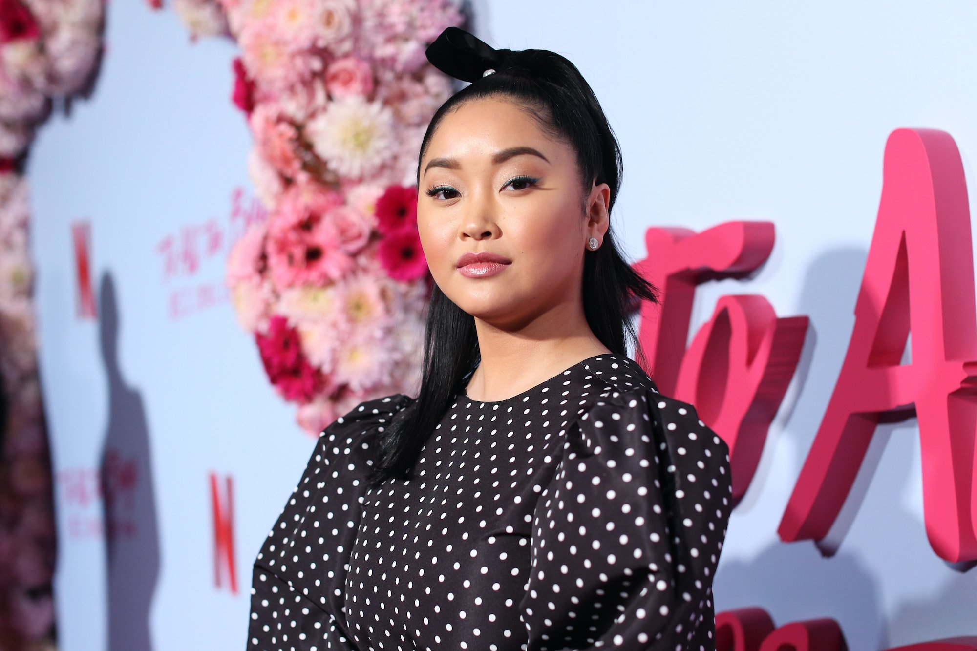 Lana Condor smiling in front of a blue and pink background