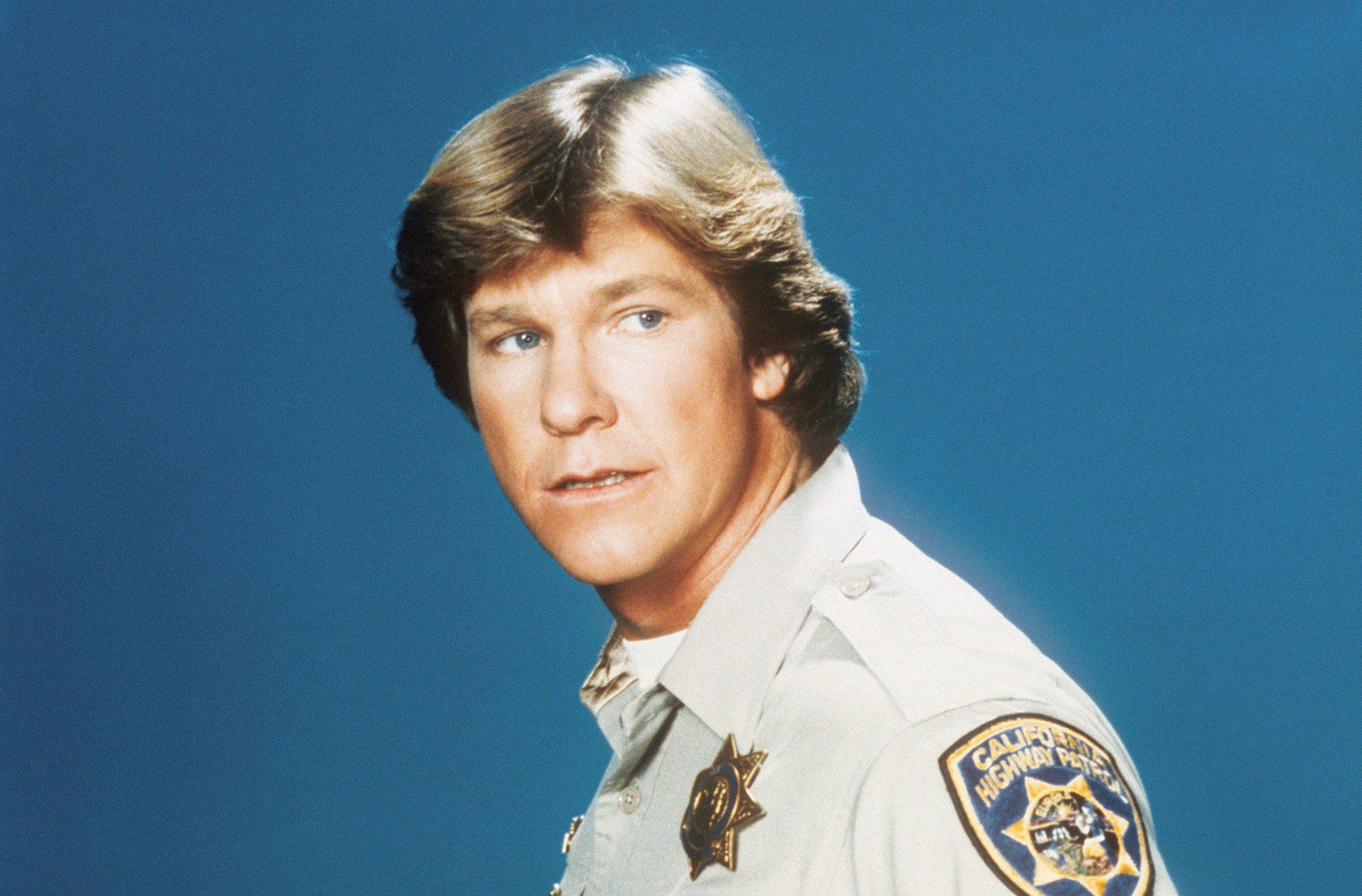 Larry Wilcox as Officer Jon Baker looking off camera in front of a blue background