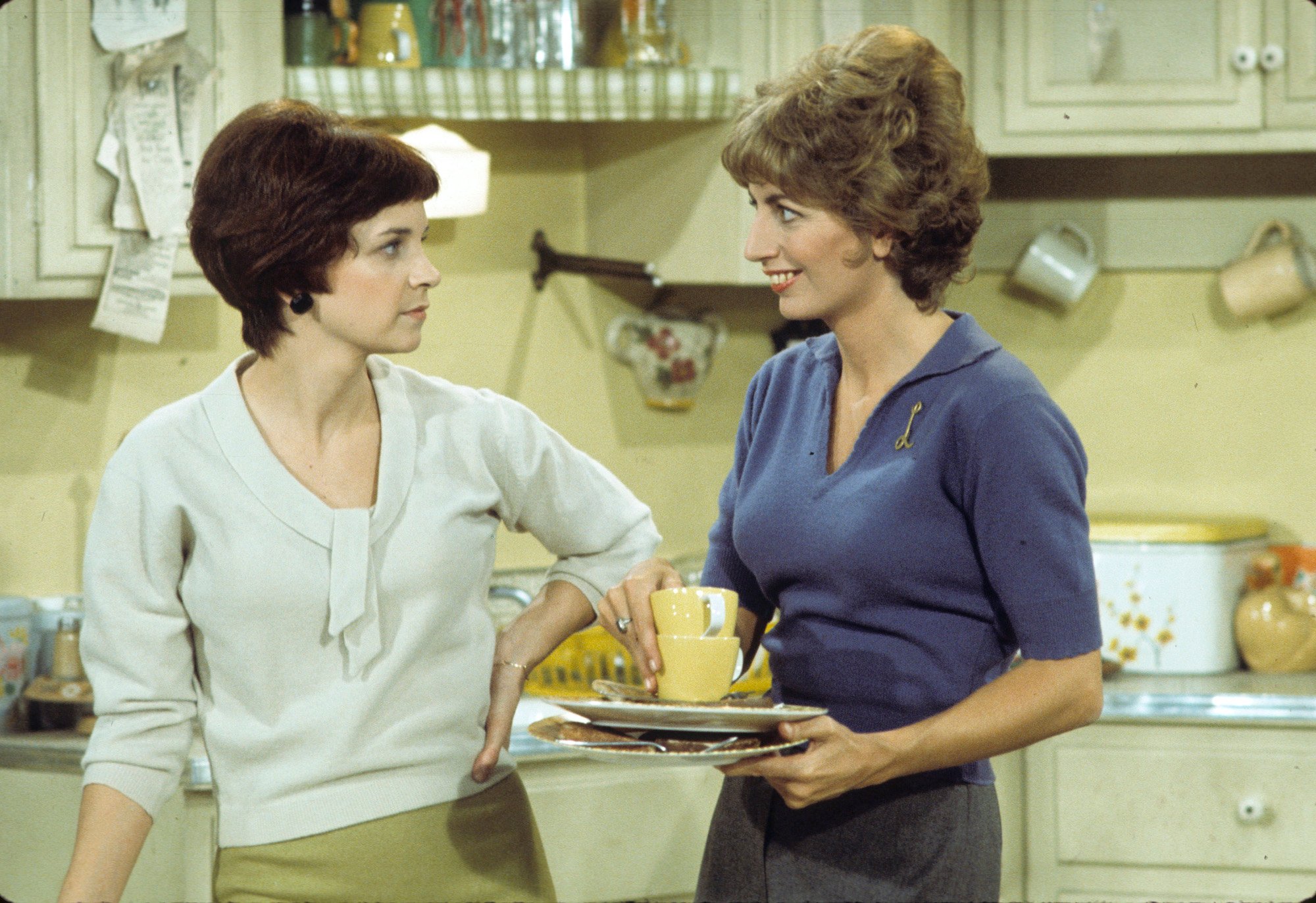(L-R) Cindy Williams and Penny Marshall smiling, standing in a kitchen