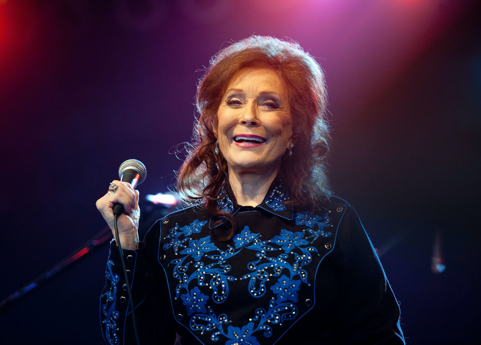 Loretta Lynn smiling on stage, holding a microphone