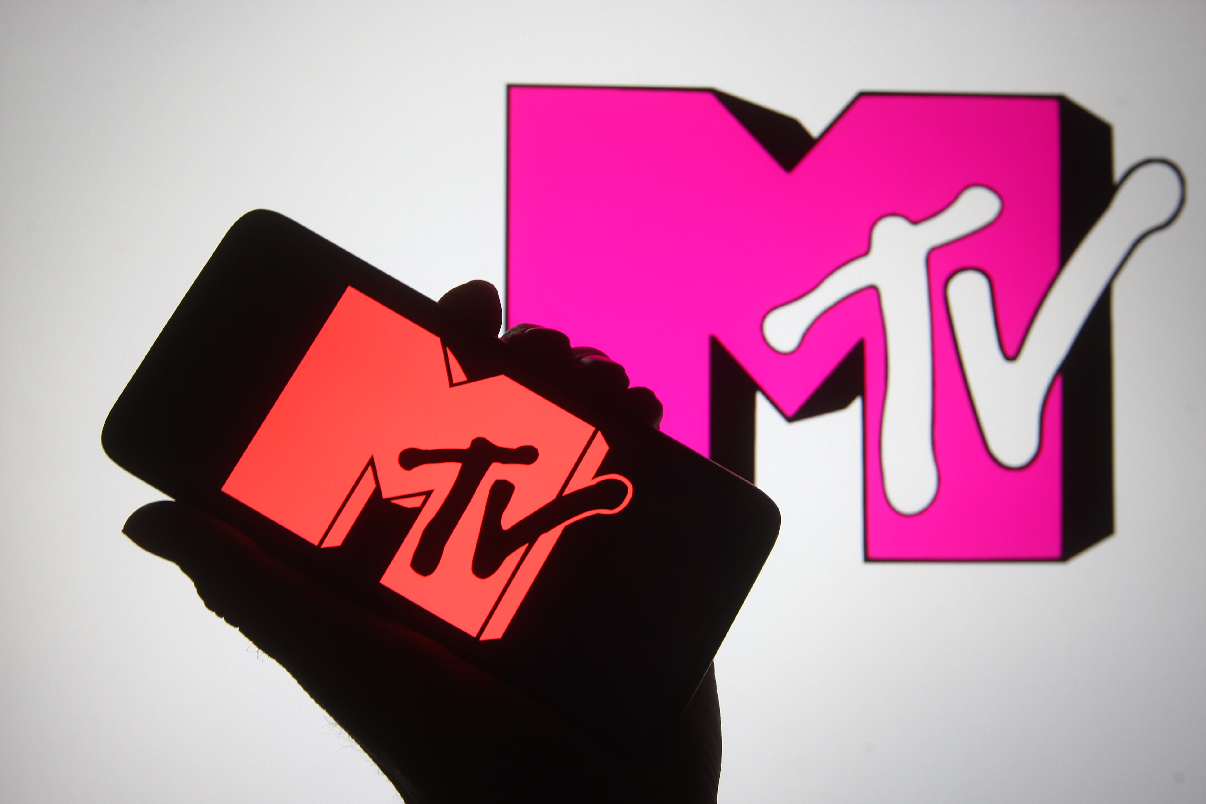 In this photo illustration a silhouette hand is seen holding a smartphone with MTV channel logo on its screen