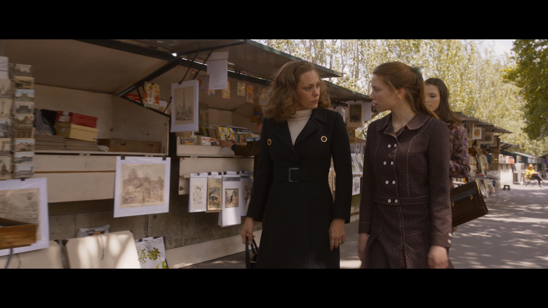 Two women walking by bouquinistes in Paris in Madame Claude