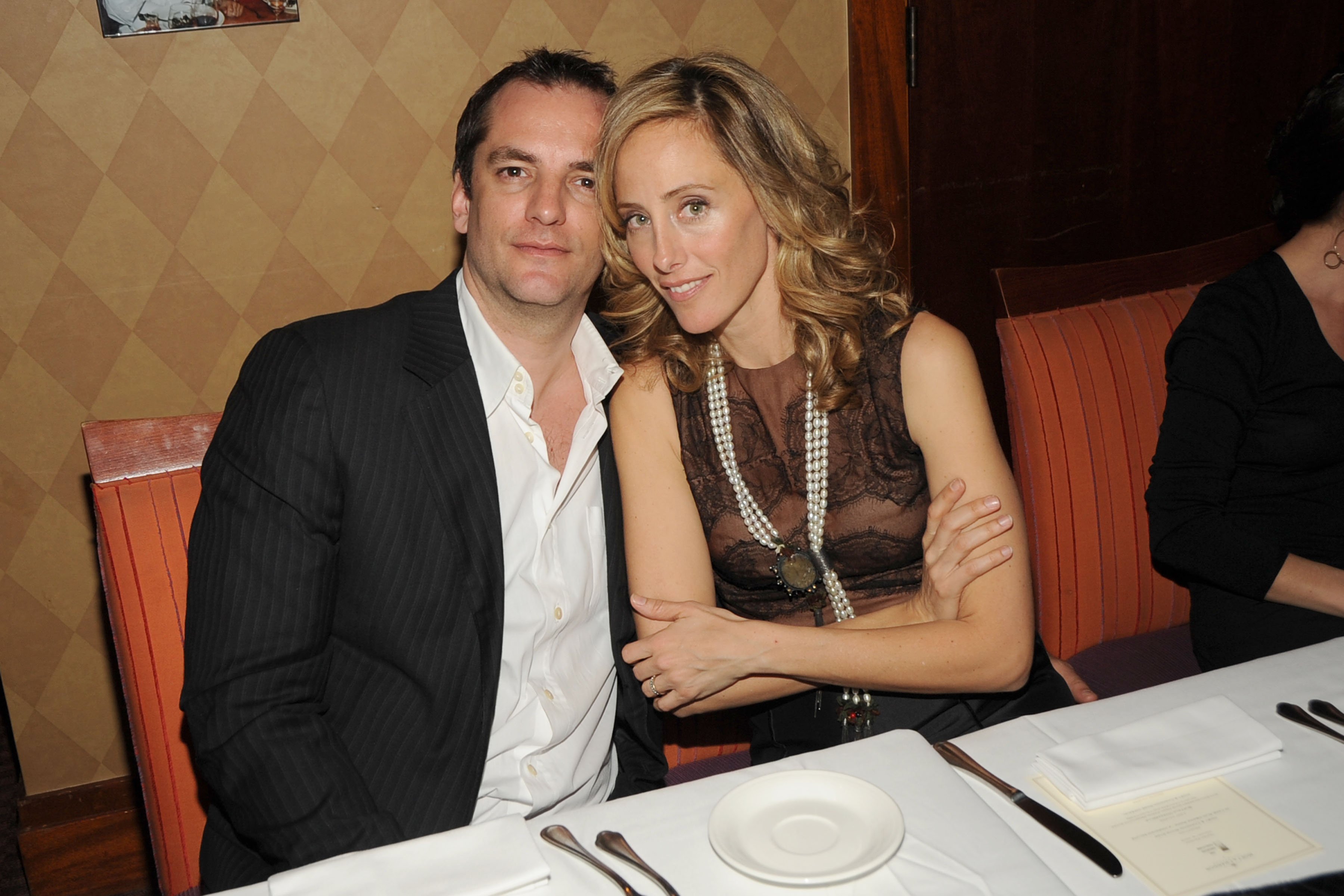Manu Boyer in a dark jacket and white shirt and wife 'Grey's Anatomy' star Kim Raver in a brown dress, sitting at a table as they attend MOET & CHANDON and 10 CANE RUM Private Dinner for THE CREATIVE COALITION at Teatro Goldoni Restaurant
