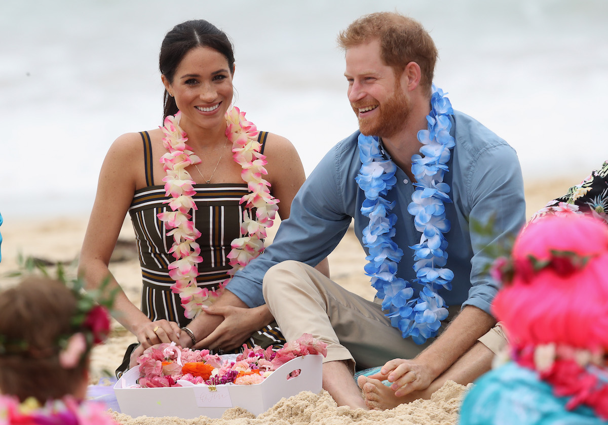Meghan Markle and Prince Harry sit on the beach in Australia holding hands and smiling