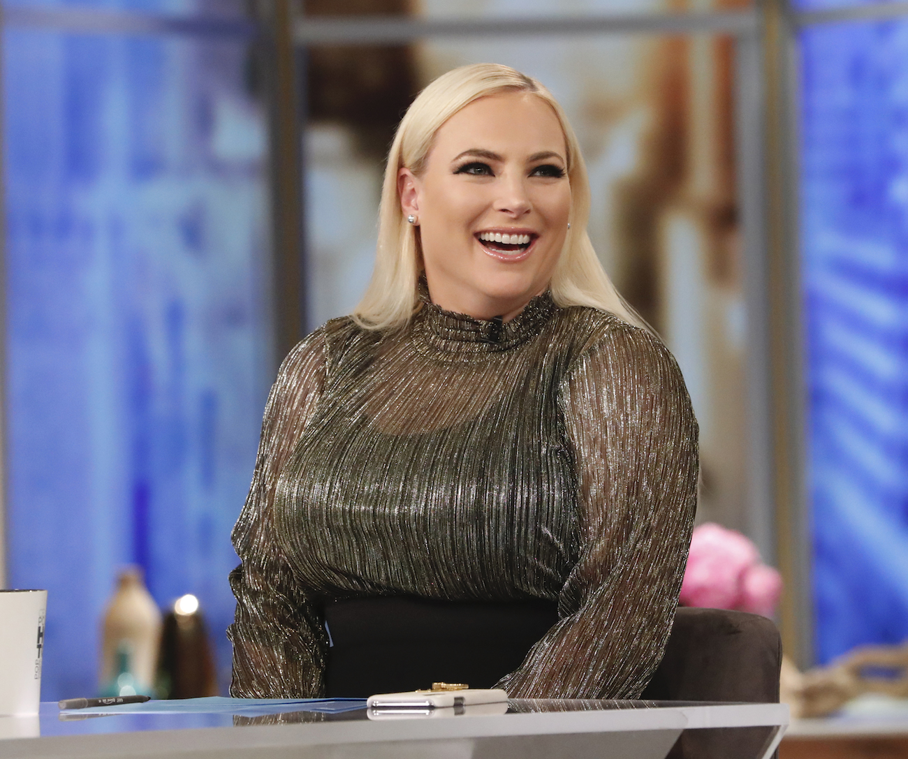 Meghan McCain is sitting at 'The View' table, smiling in a dark shimmery top