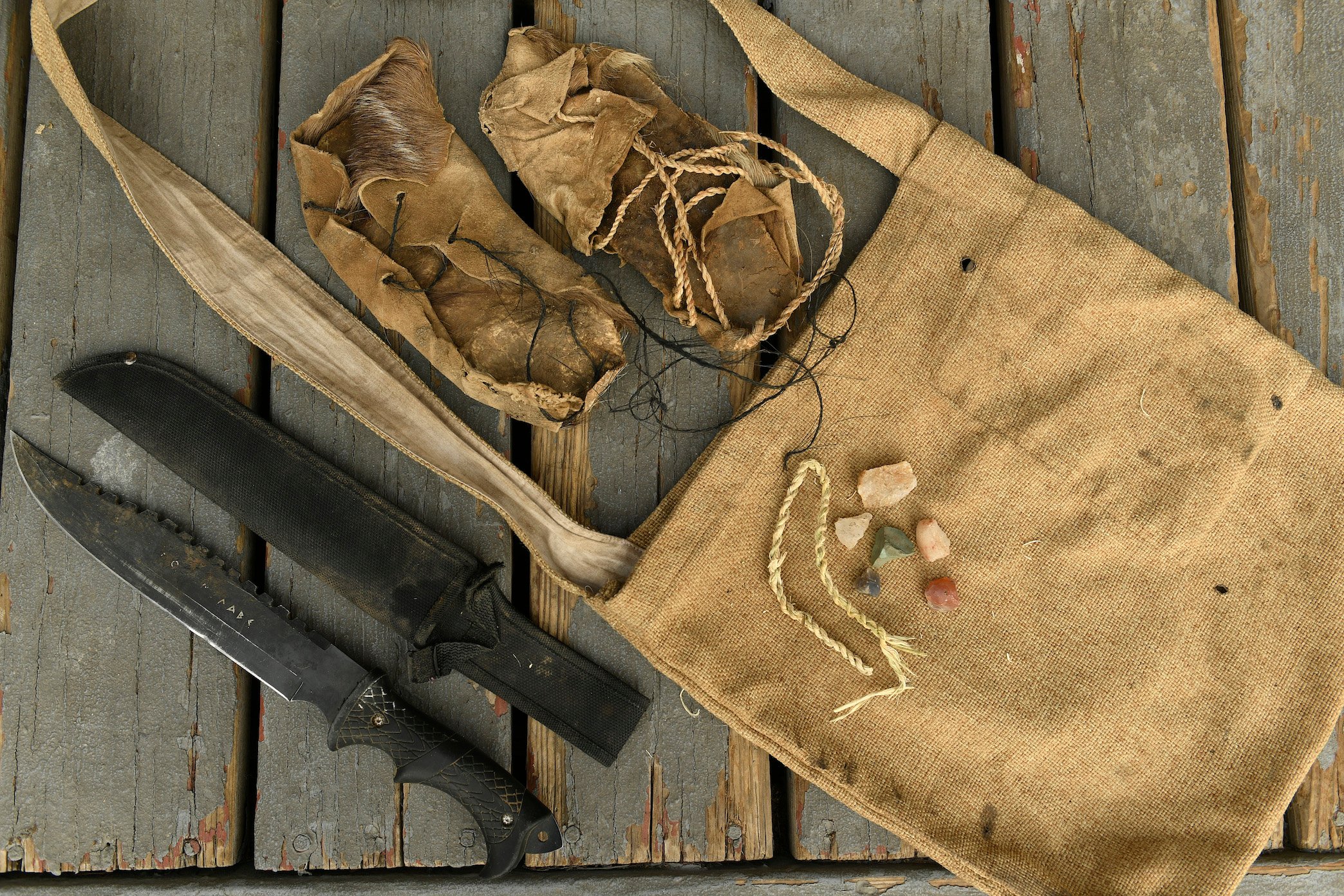 A bag, two knives, twine, and rock used by a contestant on Discovery's 'Naked and Afraid'