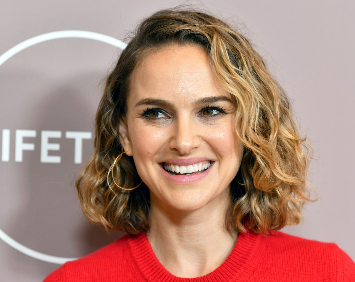 Natalie Portman with curly hair smiling and wearing a red sweater and gold earrings | Amy Sussman/FilmMagic