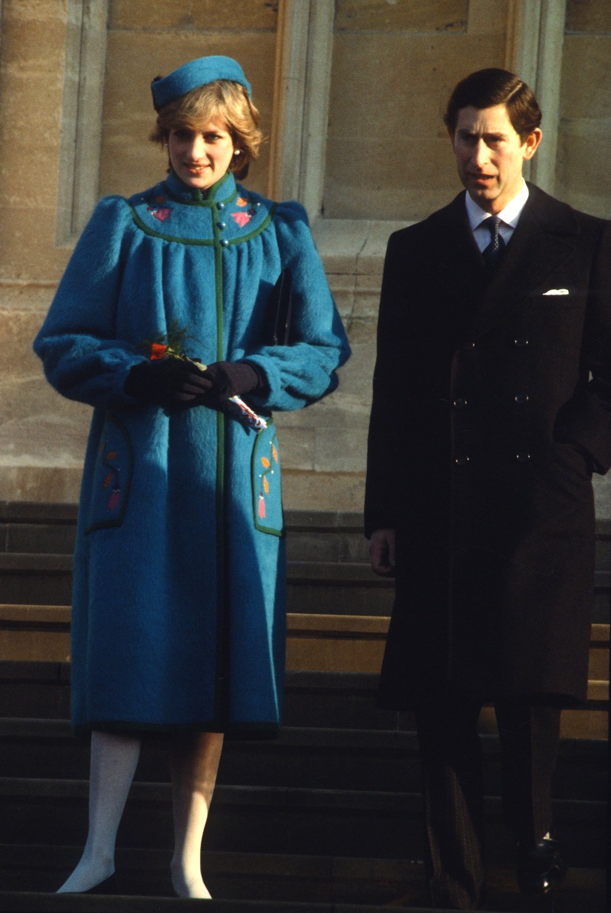 Prince Charles in suit and long jacket, and Princess Diana wearing a blue maternity coat and a matching pillbox hat, standing outside church after Christmas Day service