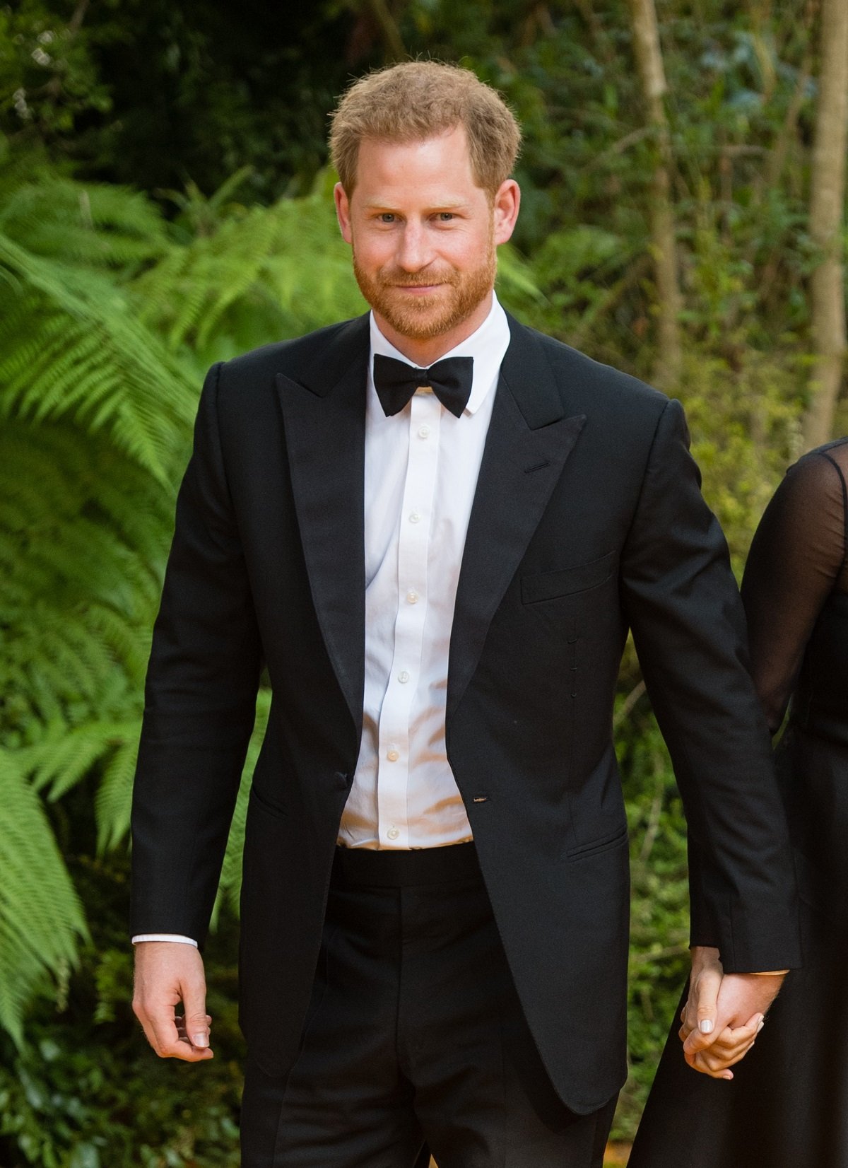 Prince Harry, Duke of Sussex, in a suit, holding hands with Meghan Markle (not fully pictured) at 'The Lion King' European Premiere at Leicester Square in London in 2019