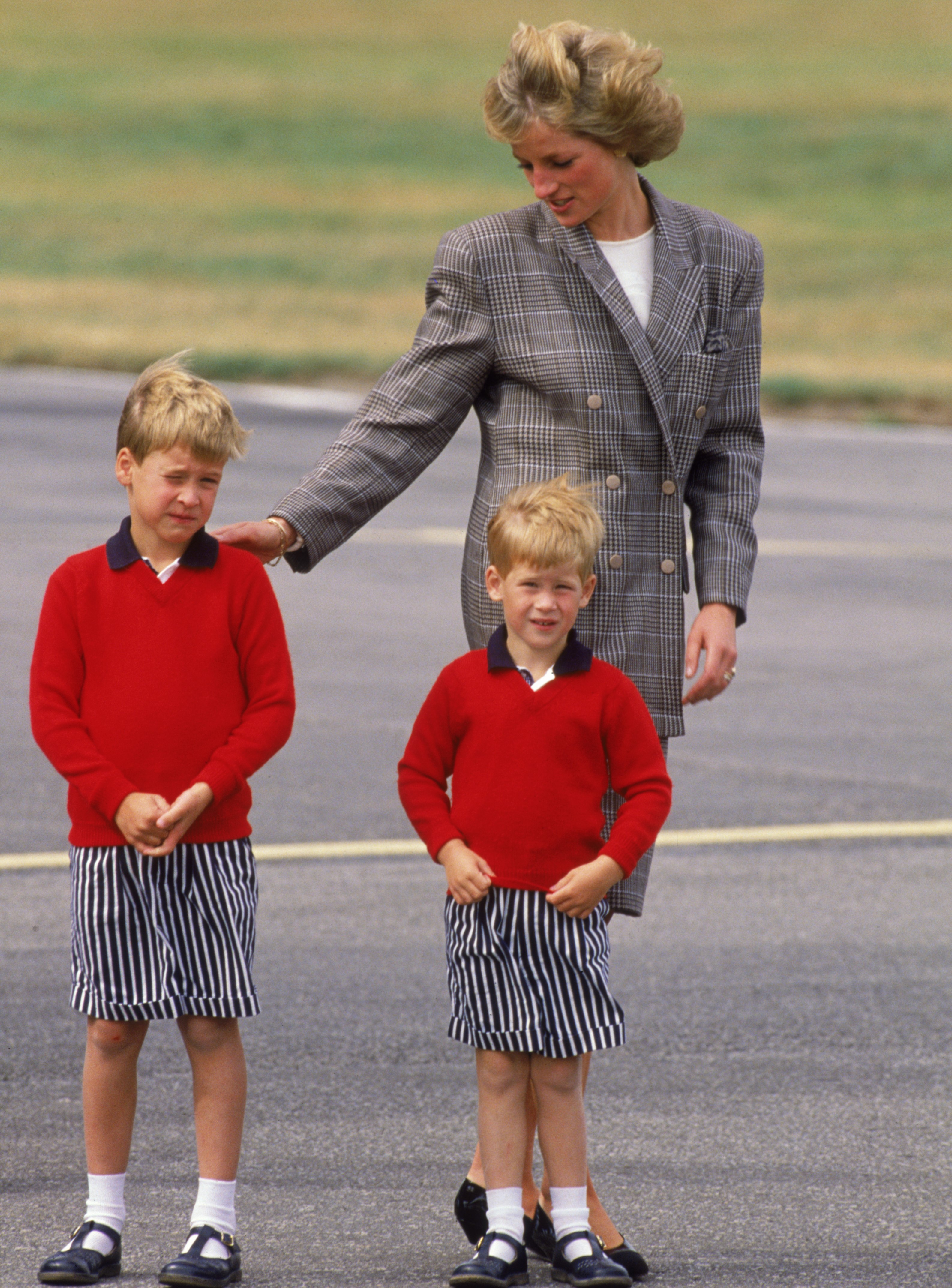 Princess Diana wearing a Mardi suit as she arrives at Aberdeen airport with her sons, William and Harry, both dressed in red sweaters and striped shorts