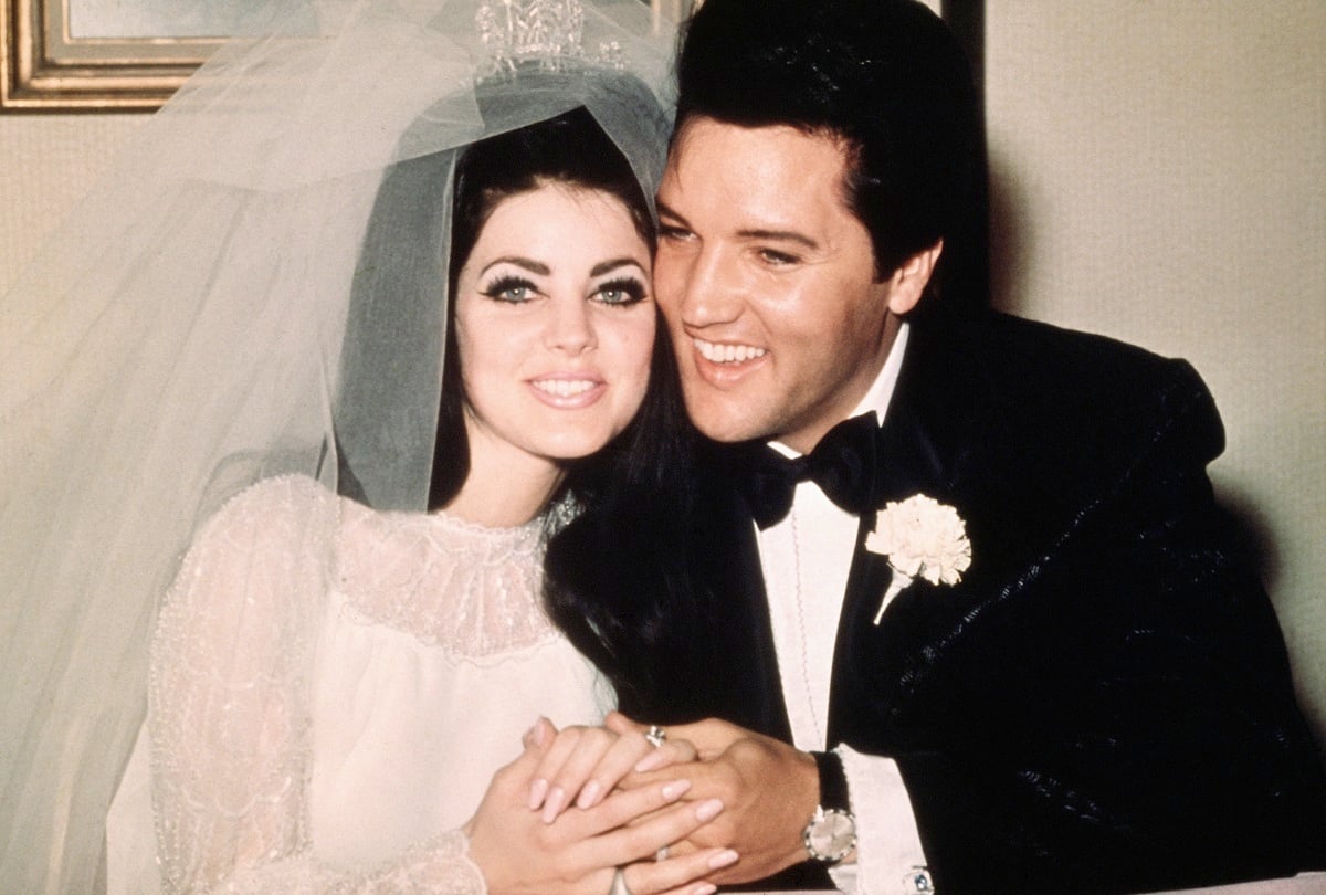 Elvis and Priscilla Presley smiling and holding hands while seated at their reception just after their wedding on May 1, 1967