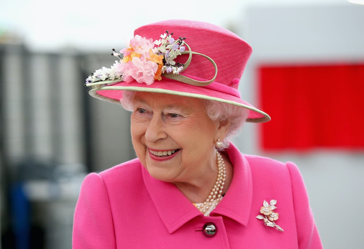 Queen Elizabeth II smiles wearing a pink hat and suit  at a royal engagement in Windsor, England