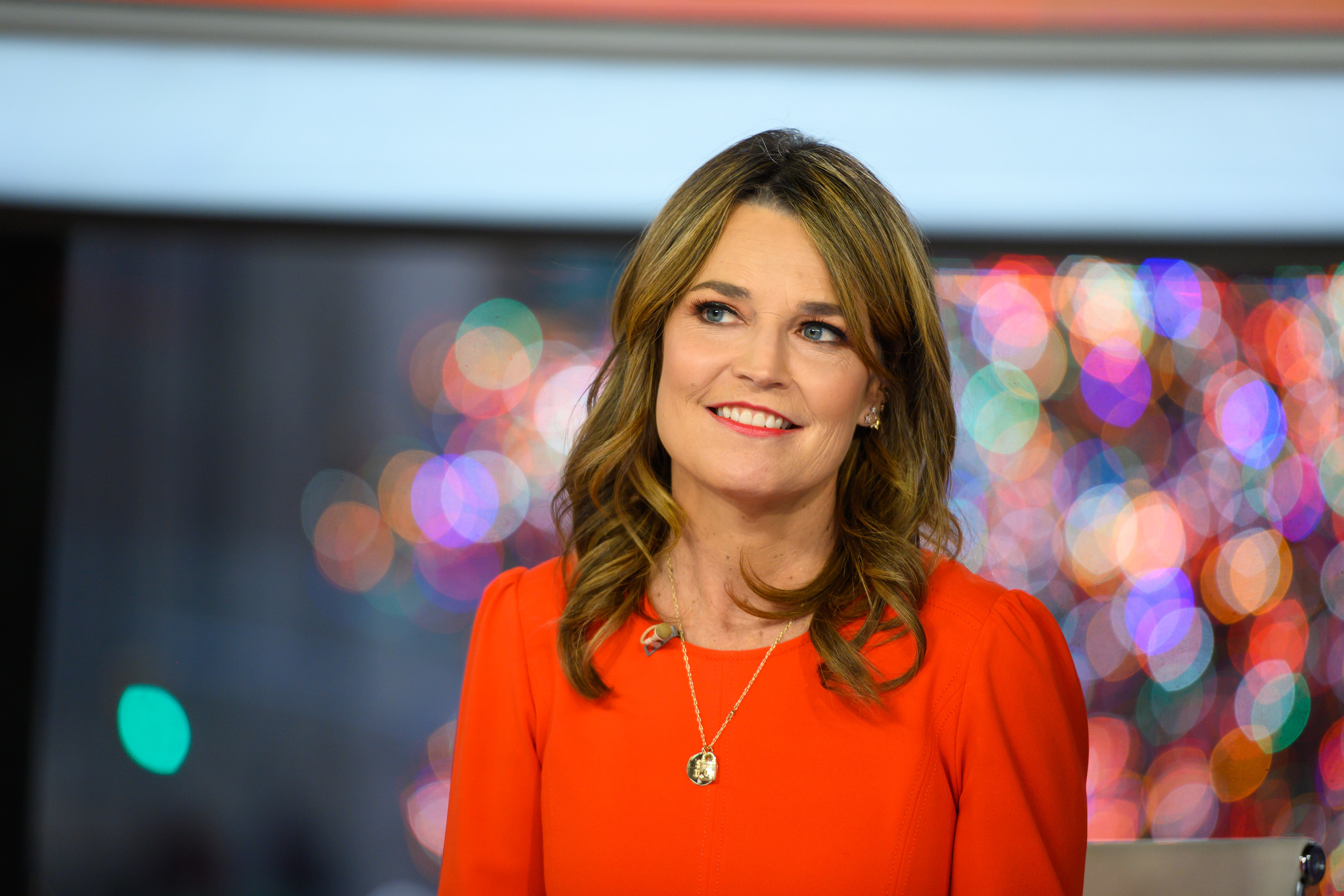 Savannah Guthrie wearing a red dress sitting at the desk of the 'Today Show'
