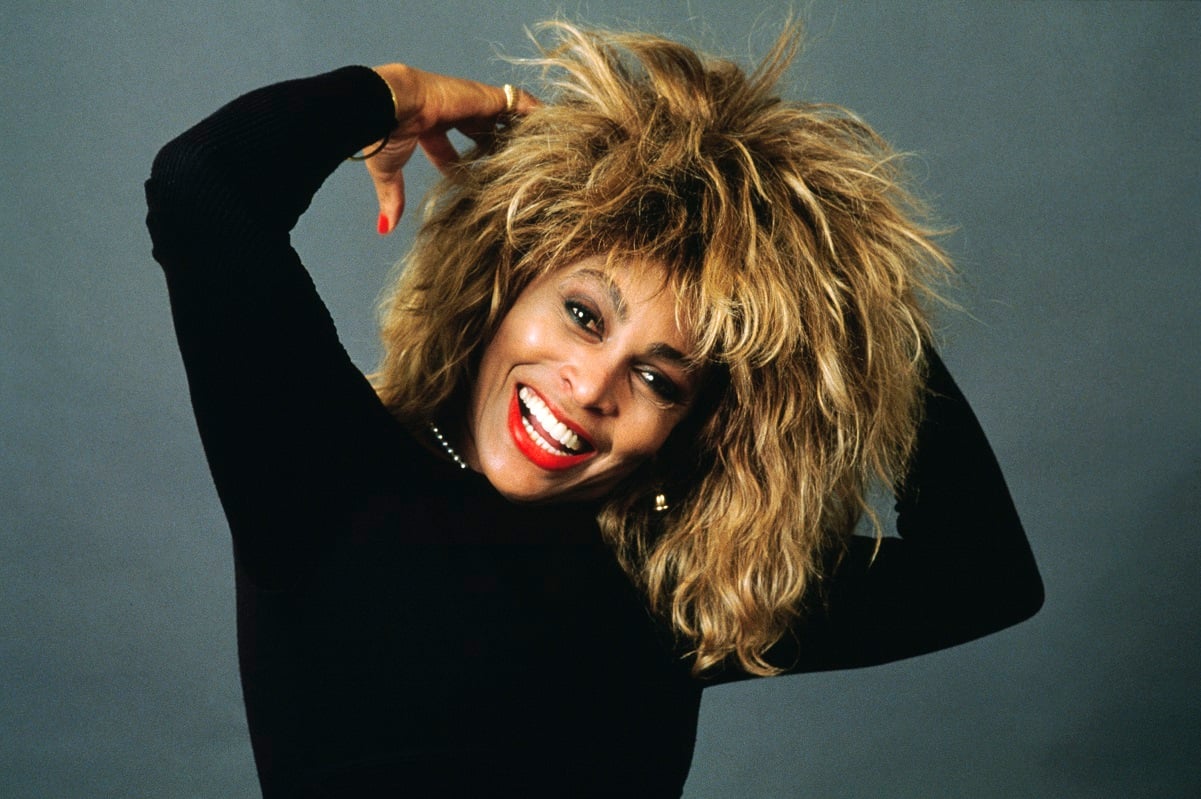 Singer Tina Turner smiling for portrait wearing a black top and pearl necklace