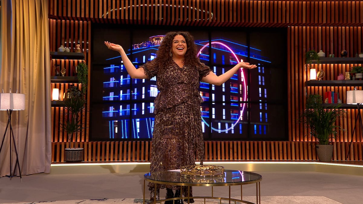 Michelle Buteau stands with her arms up on the set of 'The Circle'