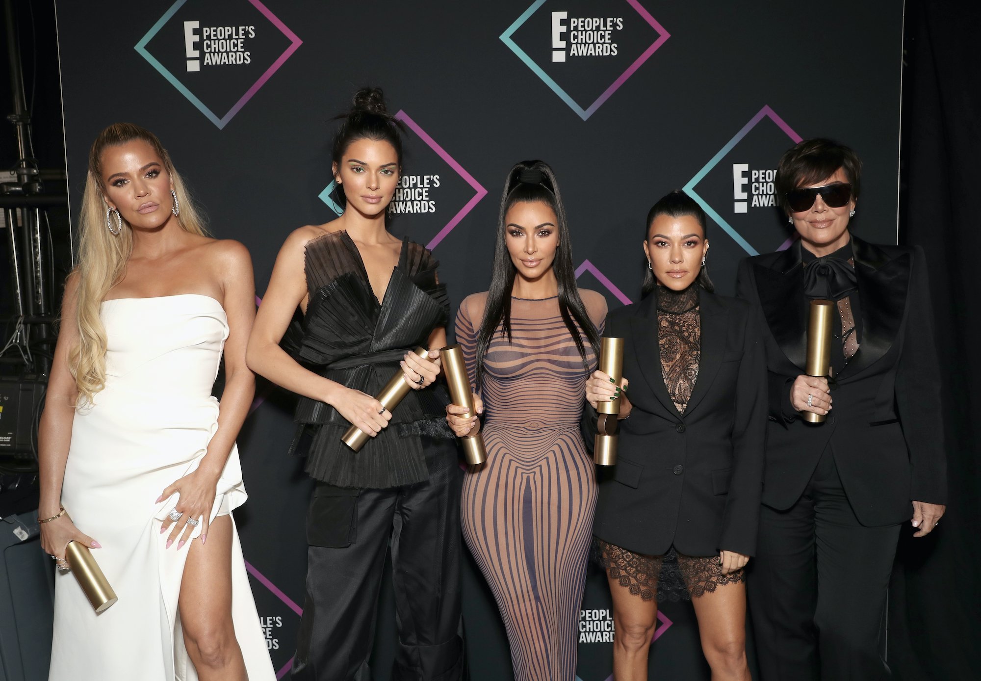 (L-R) Khloé Kardashian, Kendall Jenner, Kim Kardashian West, Kourtney Kardashian, and Kris Jenner standing in front of a black background with repeating logos