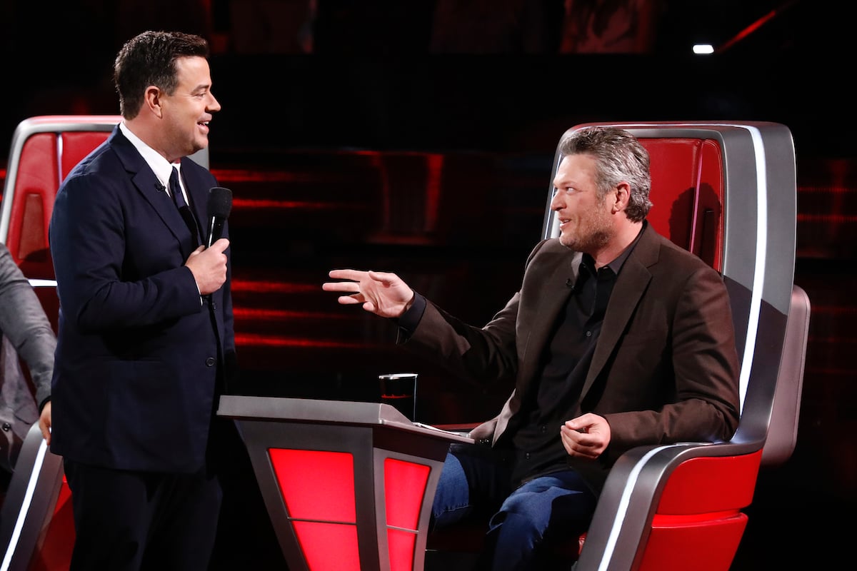Carson Daly stands in front of Blake Shelton who is sitting on set of 'The Voice'