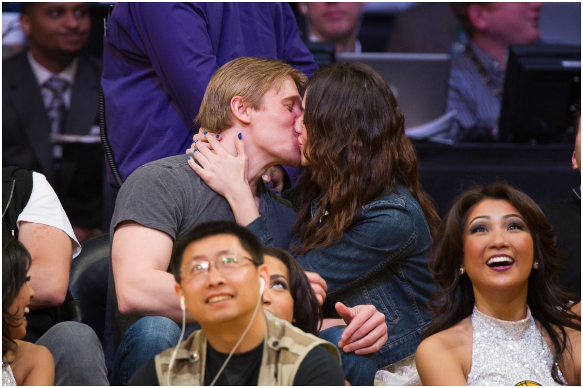 Tyler Jacob Moore and Emmy Rossum kissing at a basketball game.