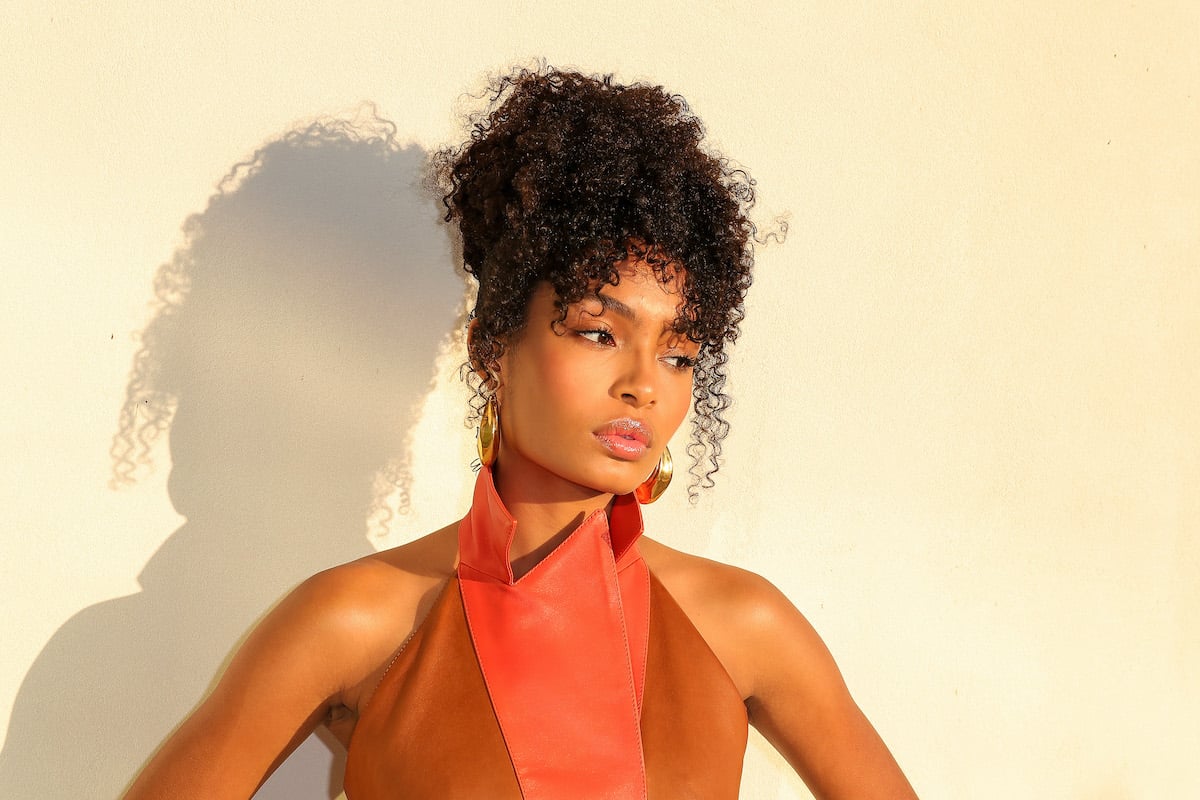 Yara Shahidi poses in front of a beige wall in a brown and pink dress | Leon Bennett/Getty Images