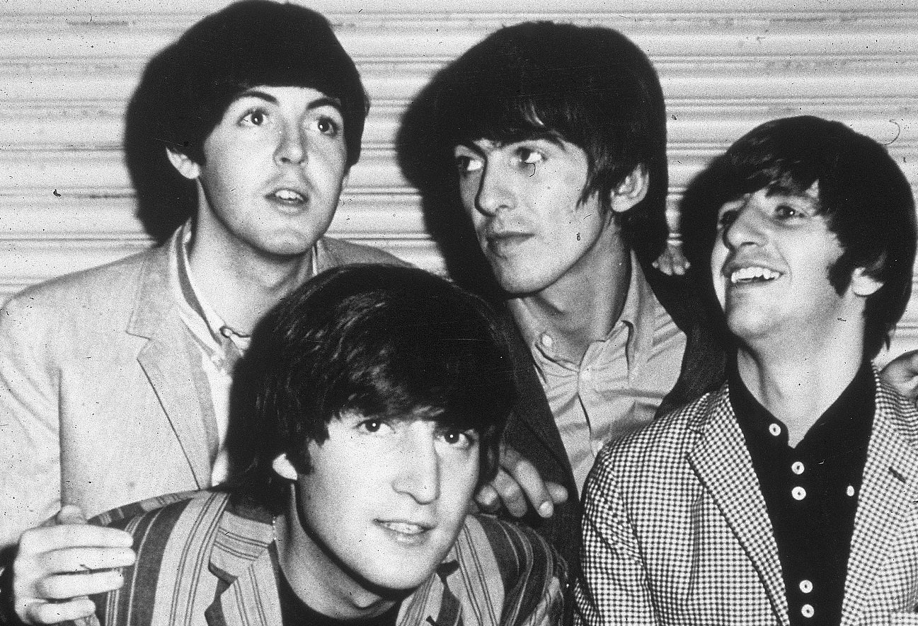 The Beatles smiling and crowding together for a photograph in 1965