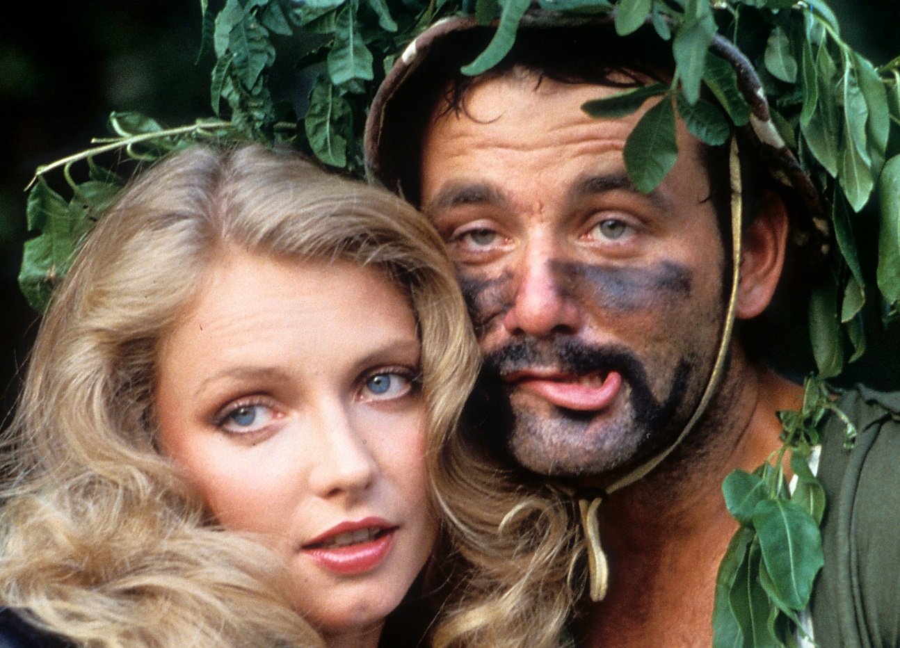 Cindy Morgan and Bill Murray with black paint smeared on his face; the two actors stand with their faces close together under a tree